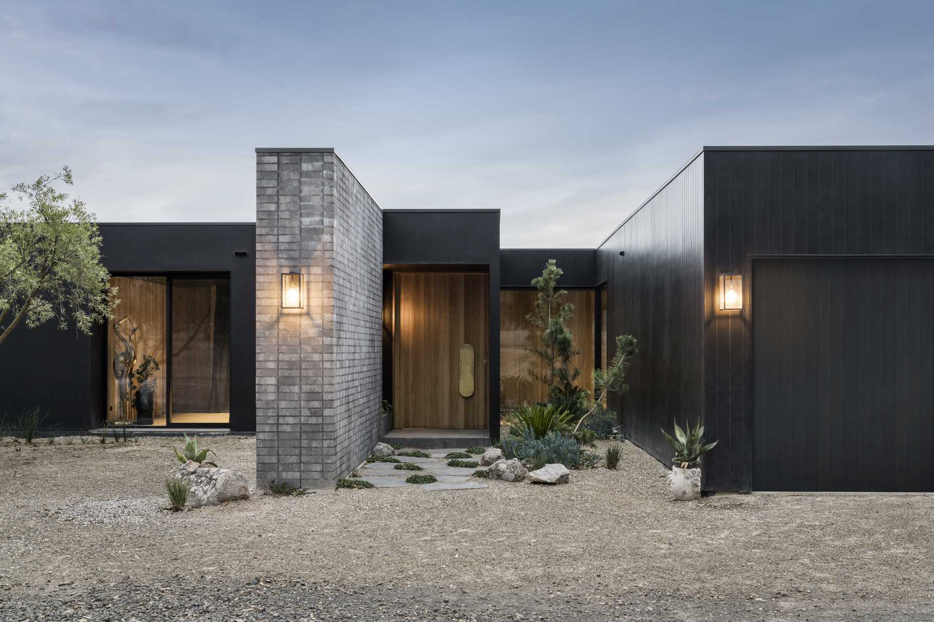 A modern home with a black exterior, includes a large wood front door with a brass handle.