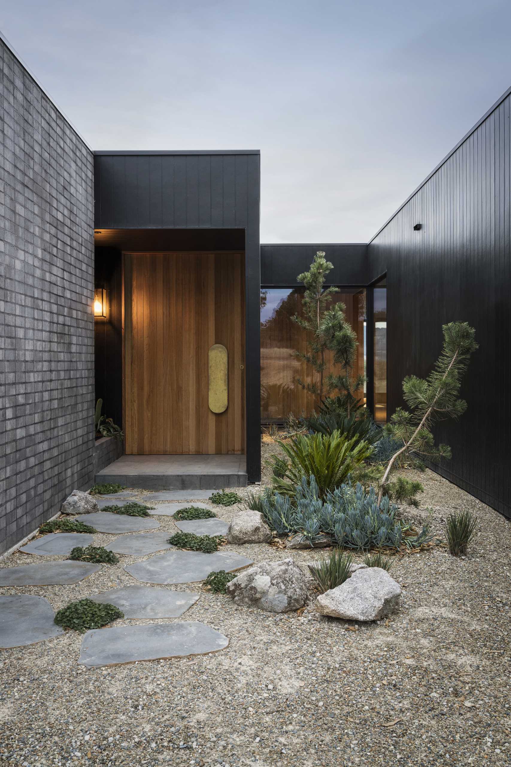 A modern home with a black exterior, includes a large wood front door with a brass handle.