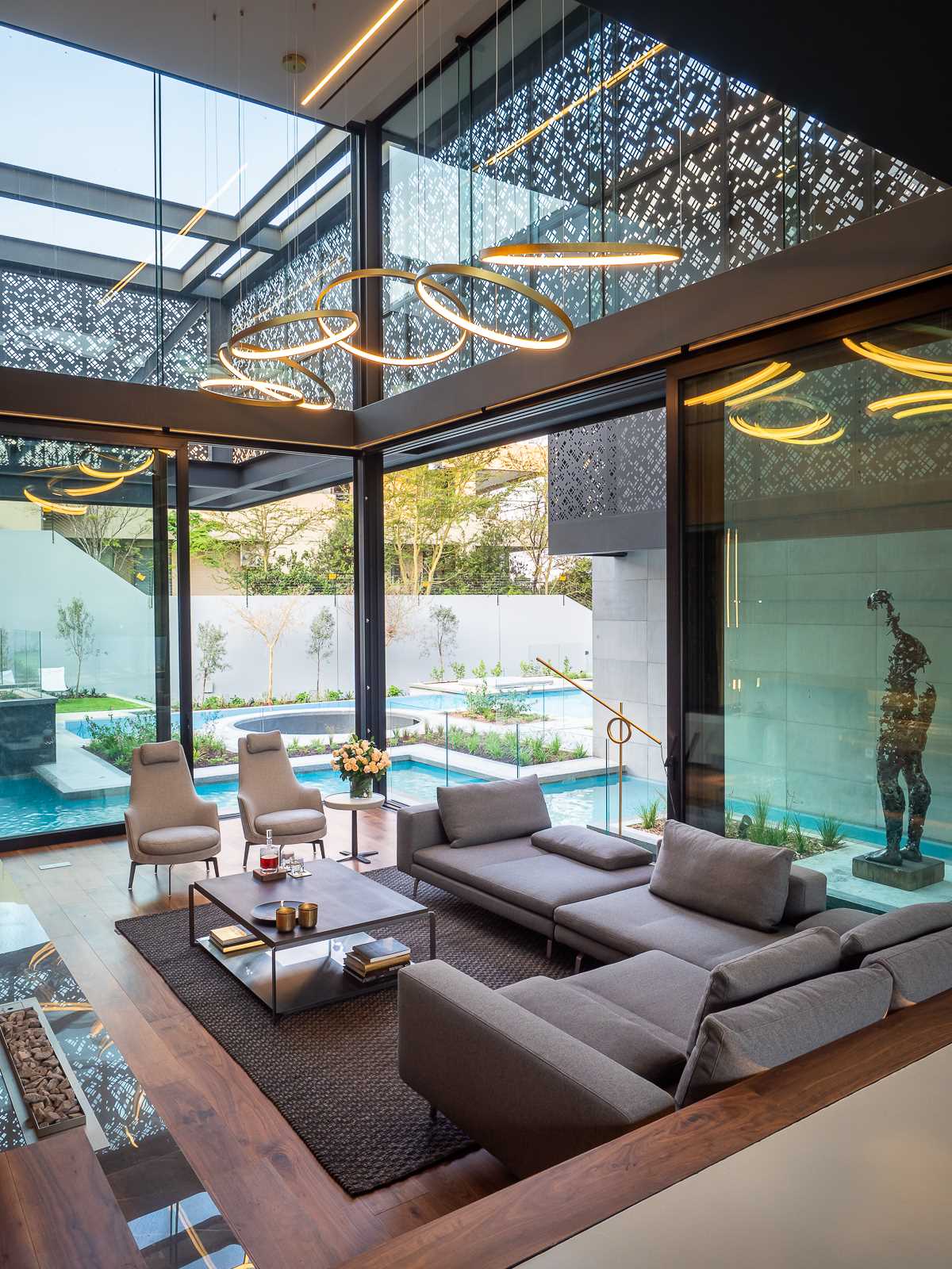 A modern house with a formal lounge includes a double height ceiling, folding metal screens, and water features.