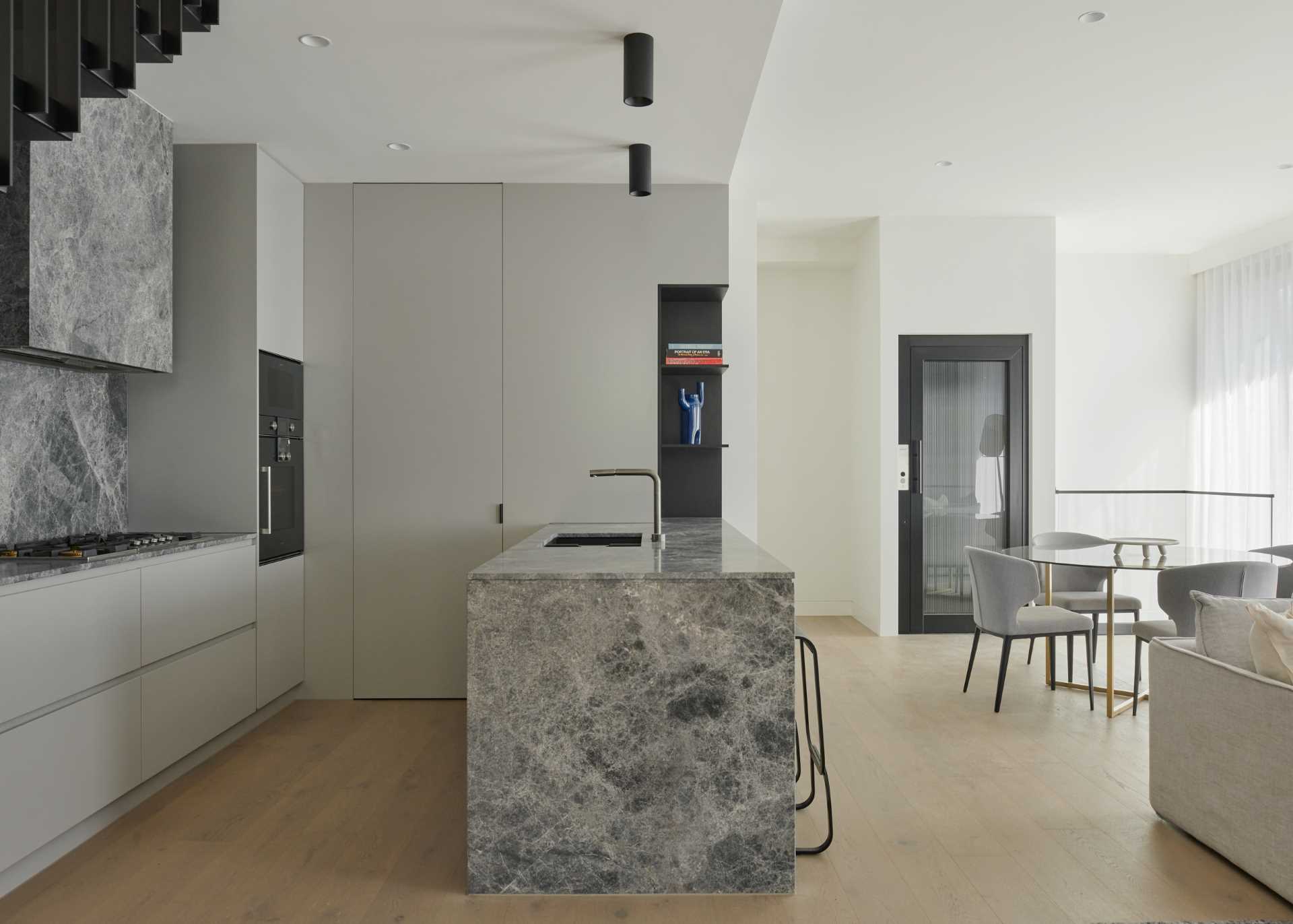 This modern kitchen, which is located underneath the stairs, and includes an island with counter seating, and minimalist hardware free cabinetry.