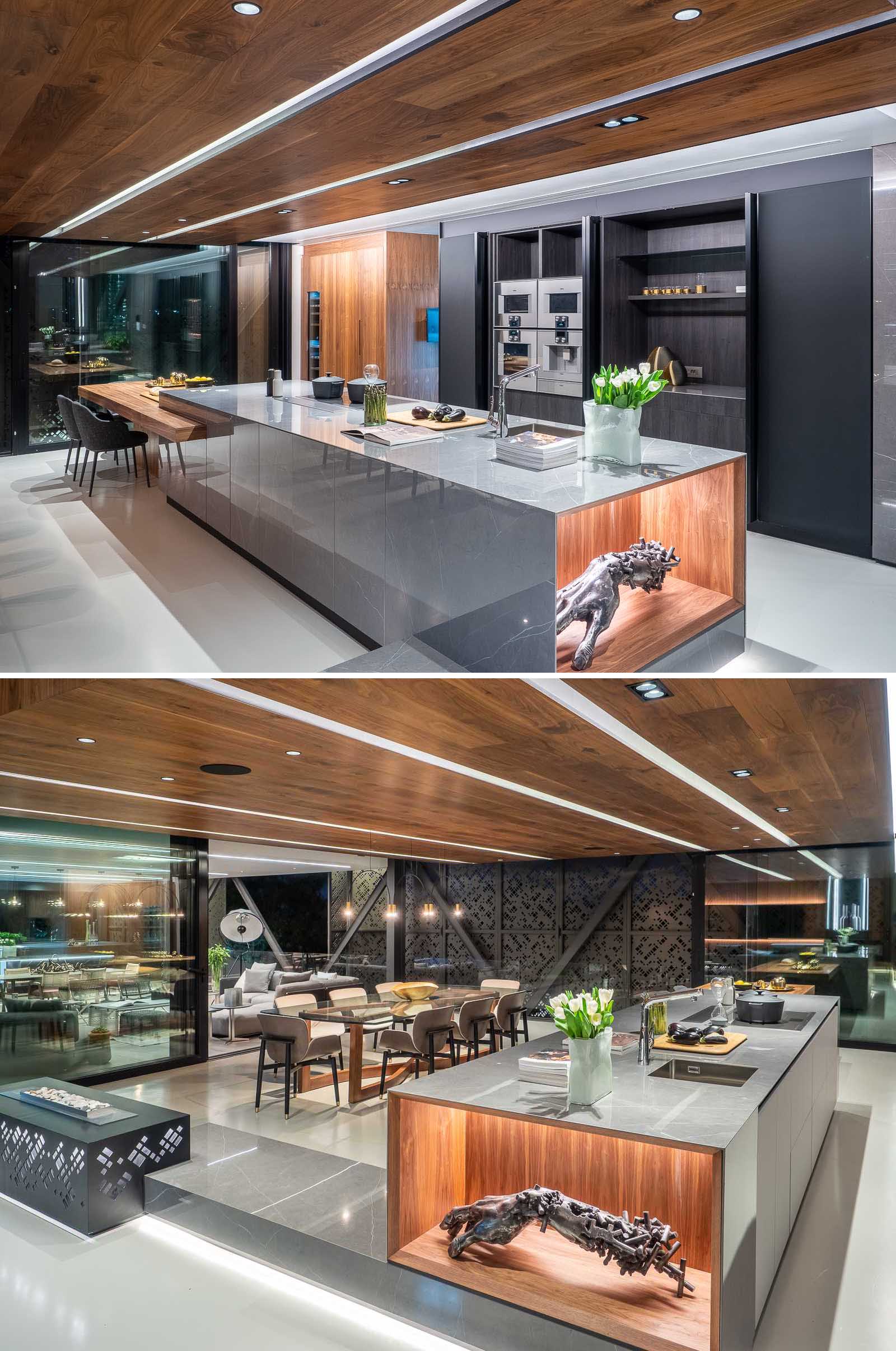In this modern kitchen, black cabinets have been combined with wood and metal accents. At the end of the island, there's a casual dining area. Adjacent to the kitchen is the main dining area with a large glass table that has a wood base.