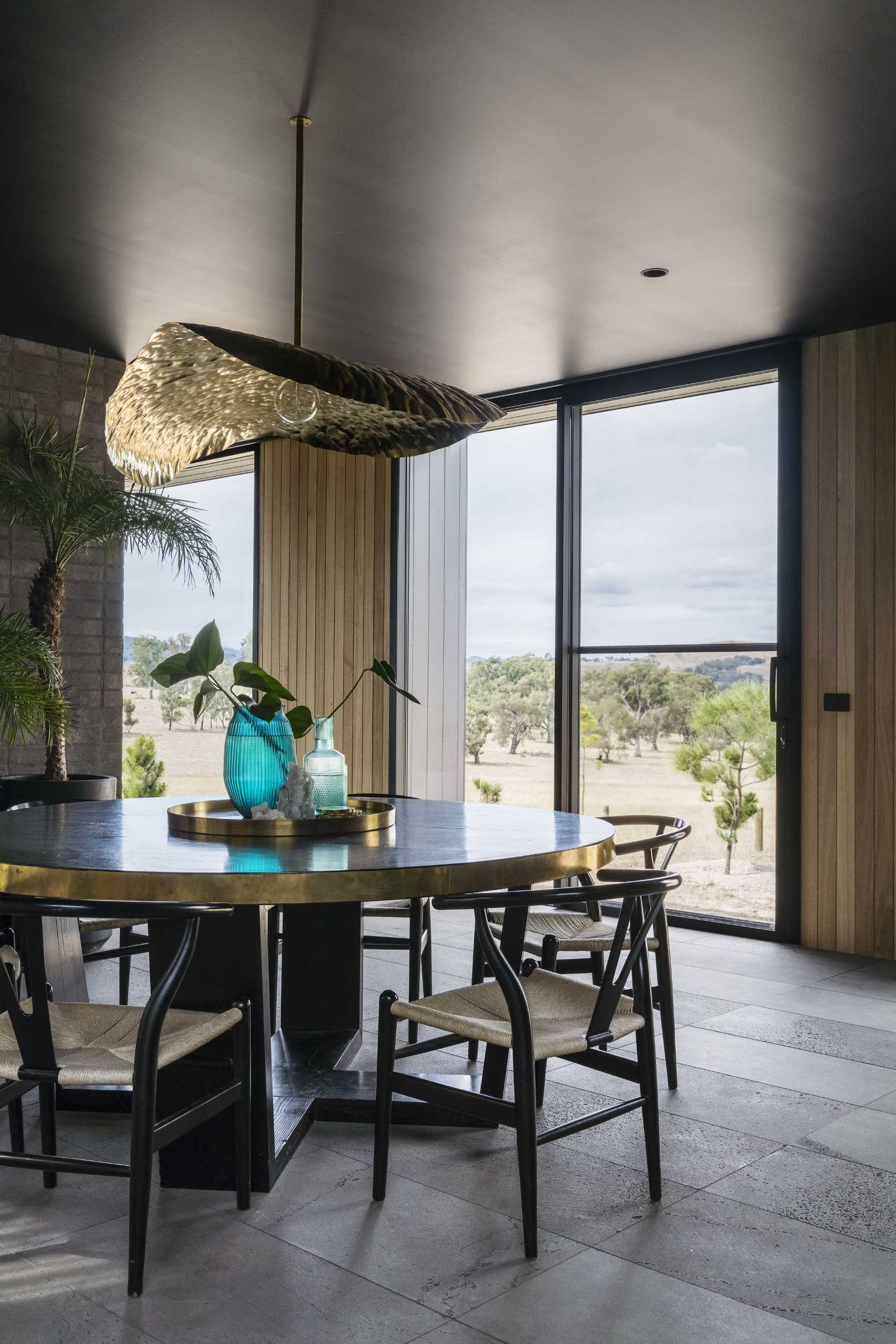 The dining room is central to the open social areas of this modern home, with a round table and a sculptural brass light fixture above.