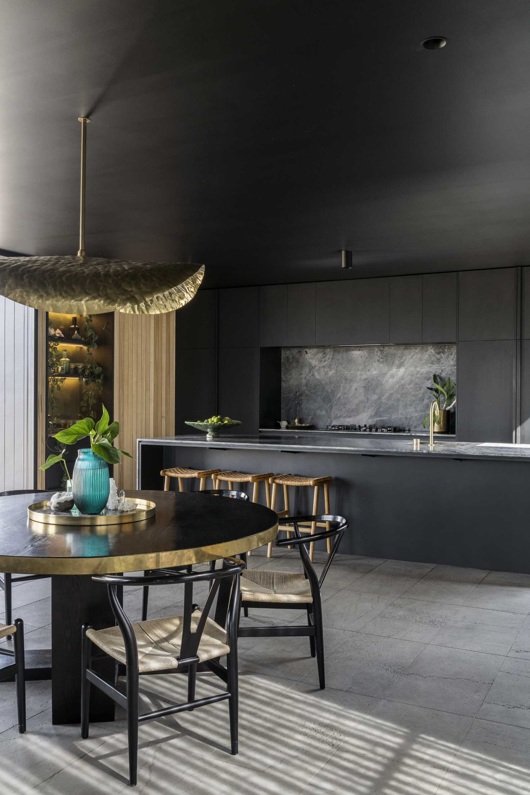 A modern black kitchen with minimalist cabinets, brass accents, and a long island.