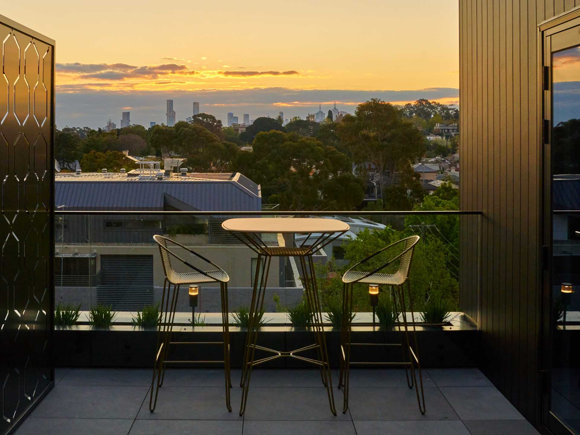 A small outdoor space with a glass railing, metal screen, and a table set for two.