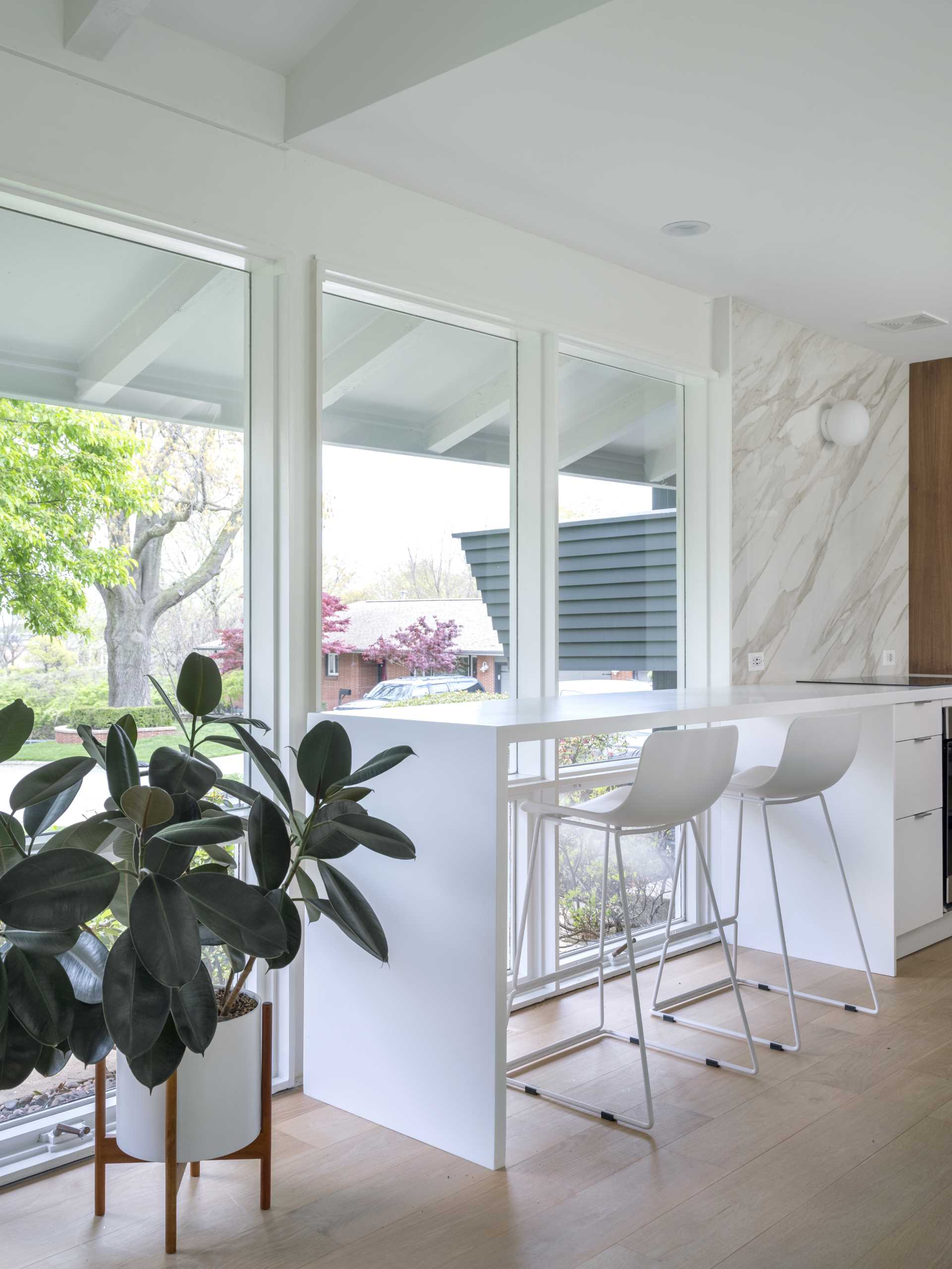 The new kitchen of this renovated mid-century modern home, is bright and open with long white countertops, wood cabinets, and a seating area by the windows.