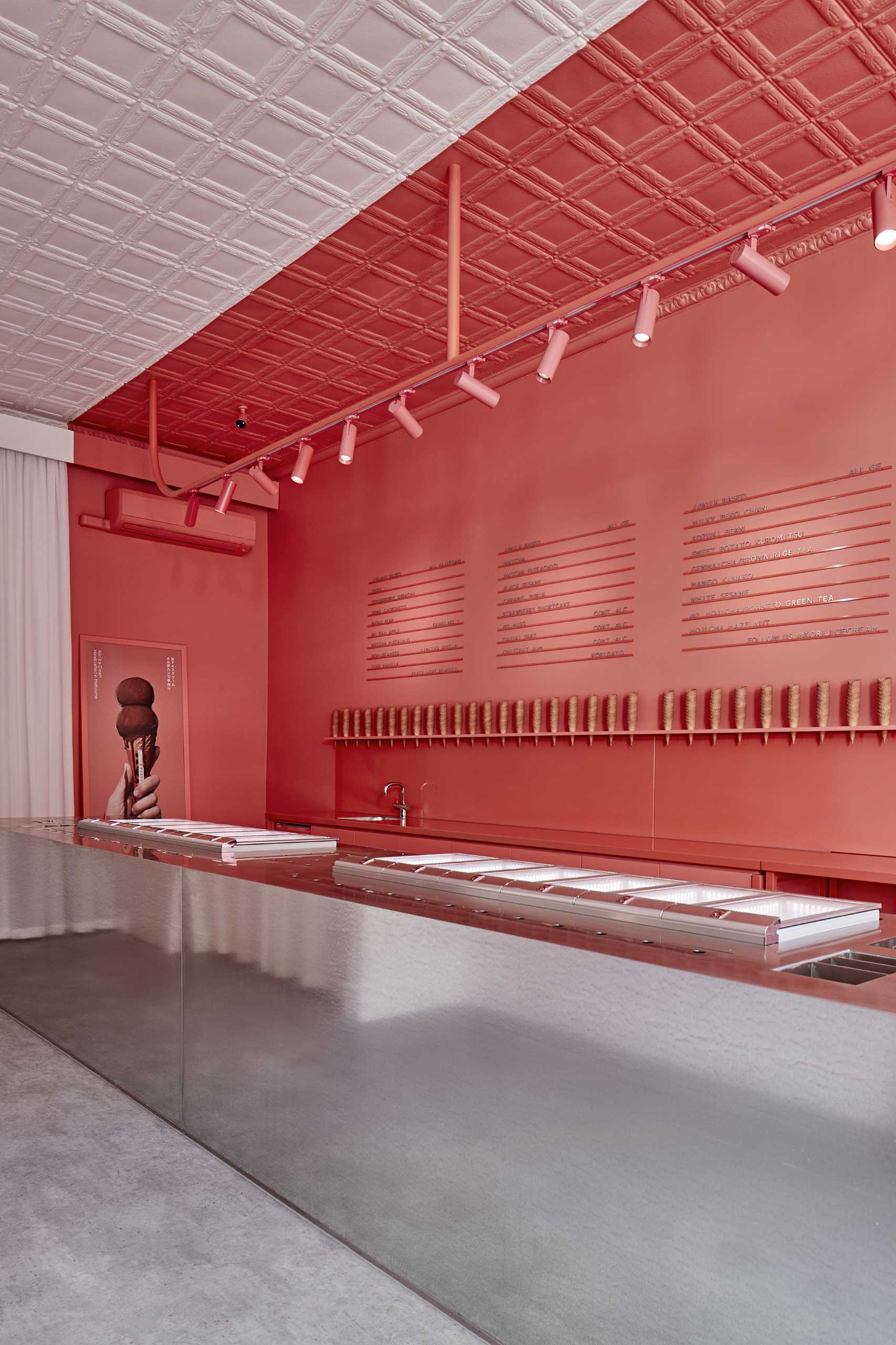 A modern ice cream shop with matte pink and white walls that includes a large steel island.
