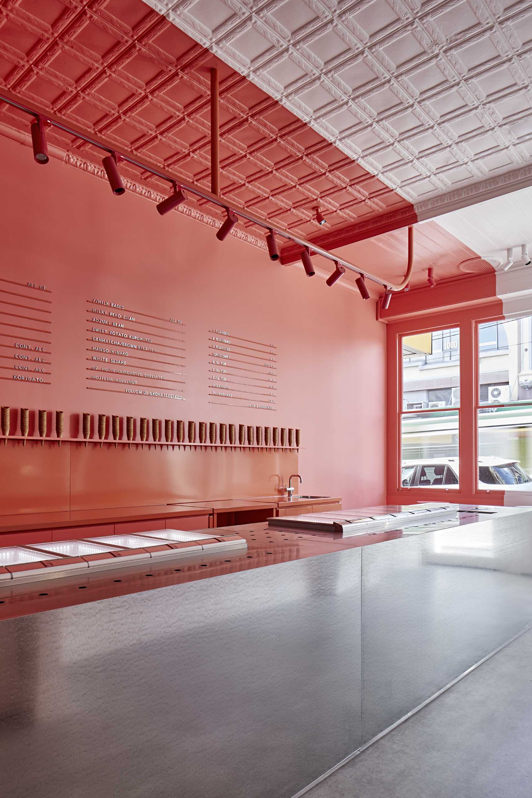 A modern ice cream shop with a matte pink and white walls that includes a large steel island.