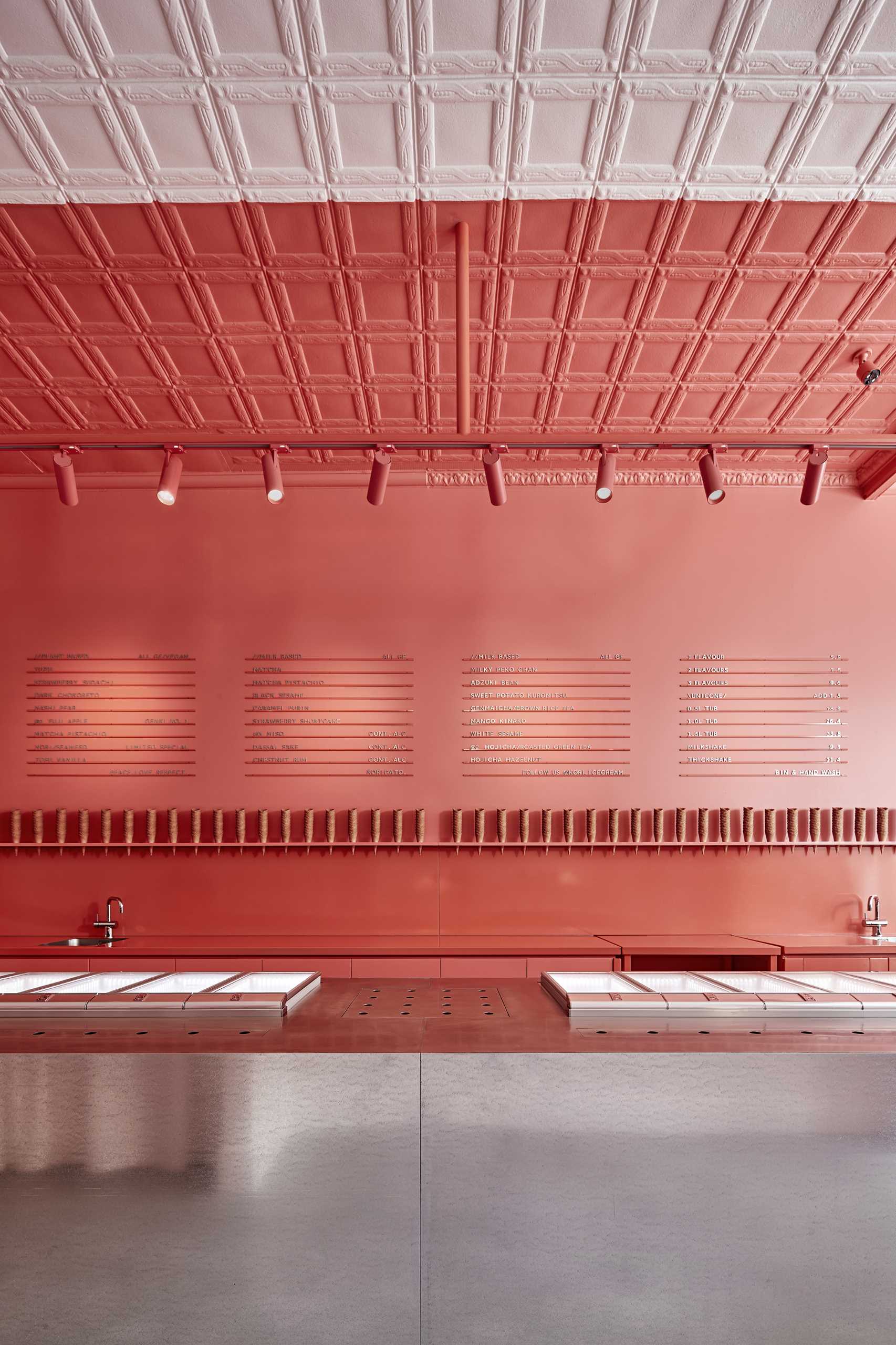 A modern ice cream shop with a matte pink and white walls that includes a minimalist menu.