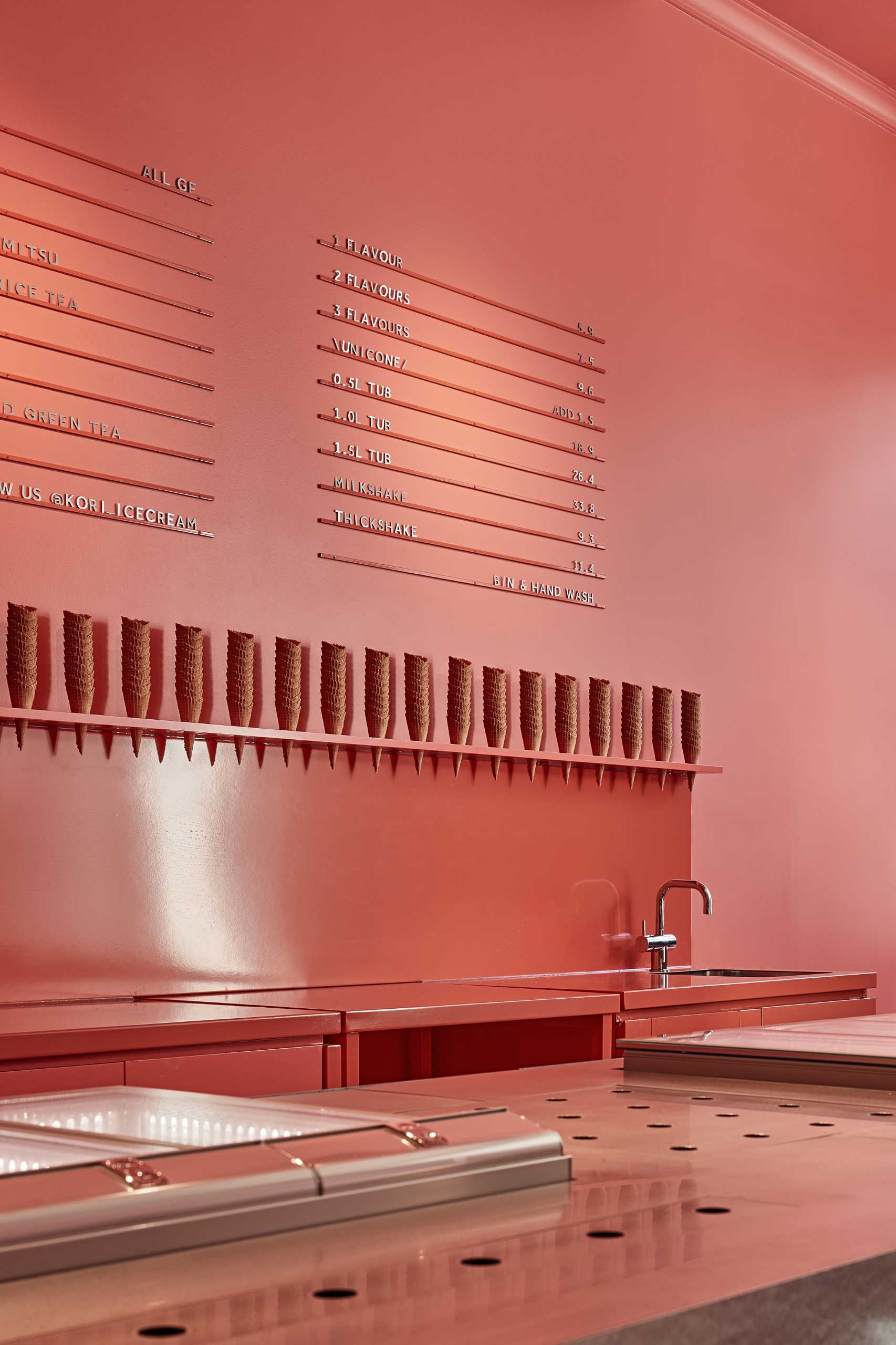 A modern ice cream shop with a matte pink wall that includes a minimalist menu.