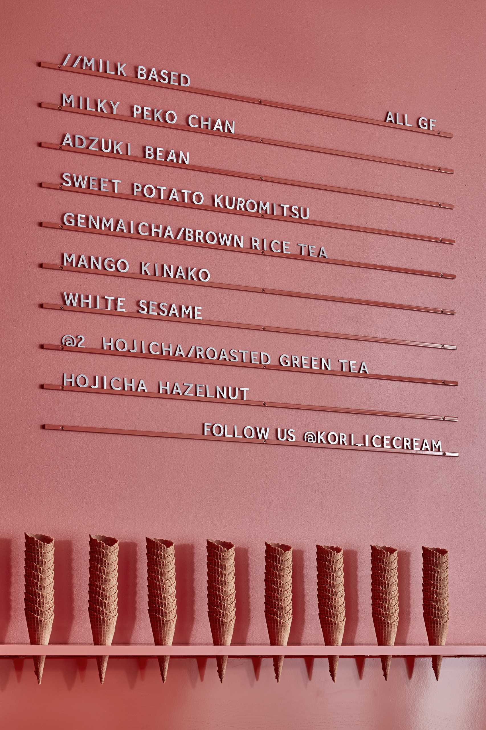 A modern ice cream shop with a matte pink wall that includes a minimalist menu.