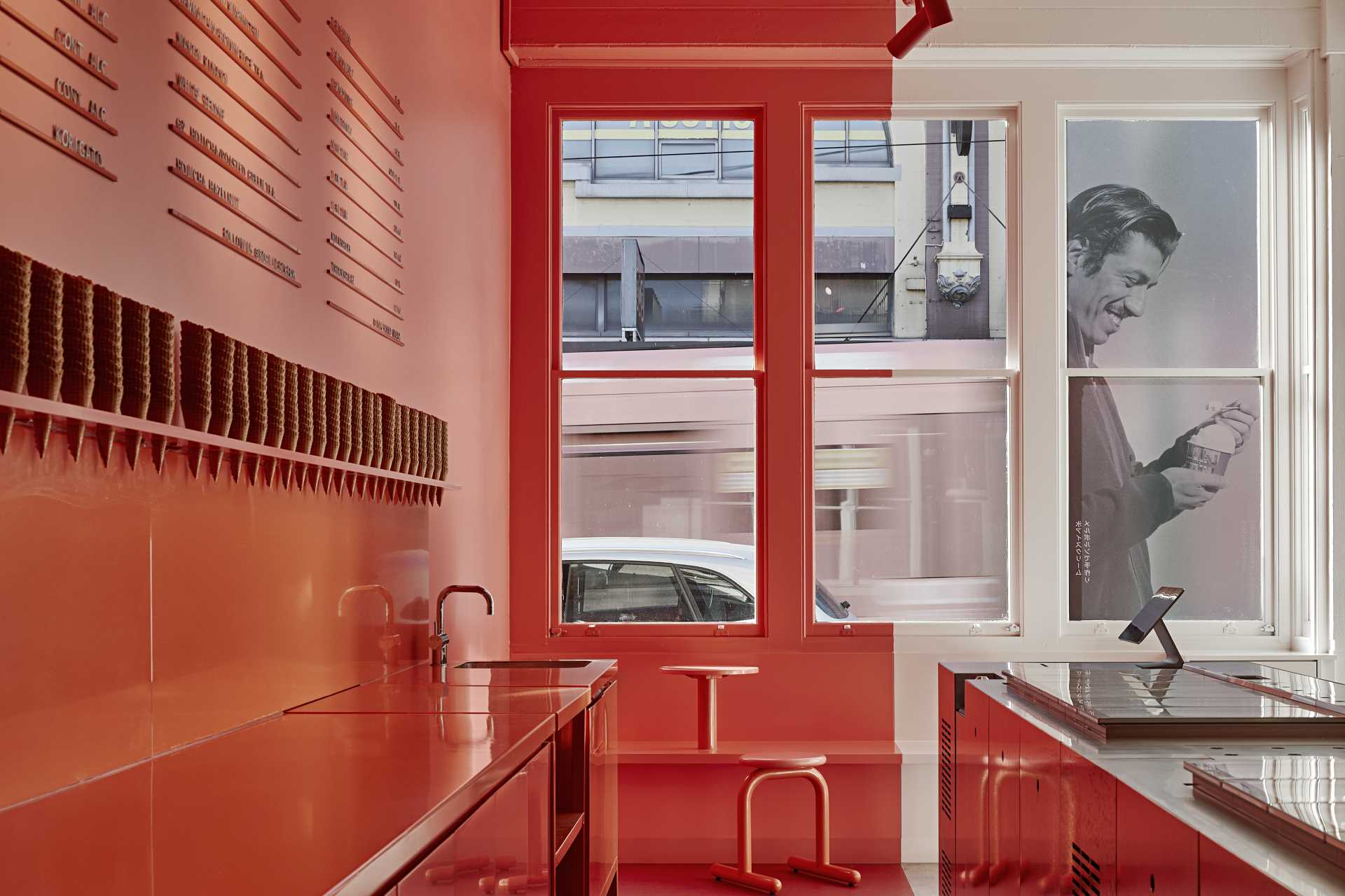 A modern ice cream shop with a matte pink and white interior, and seats by the window.