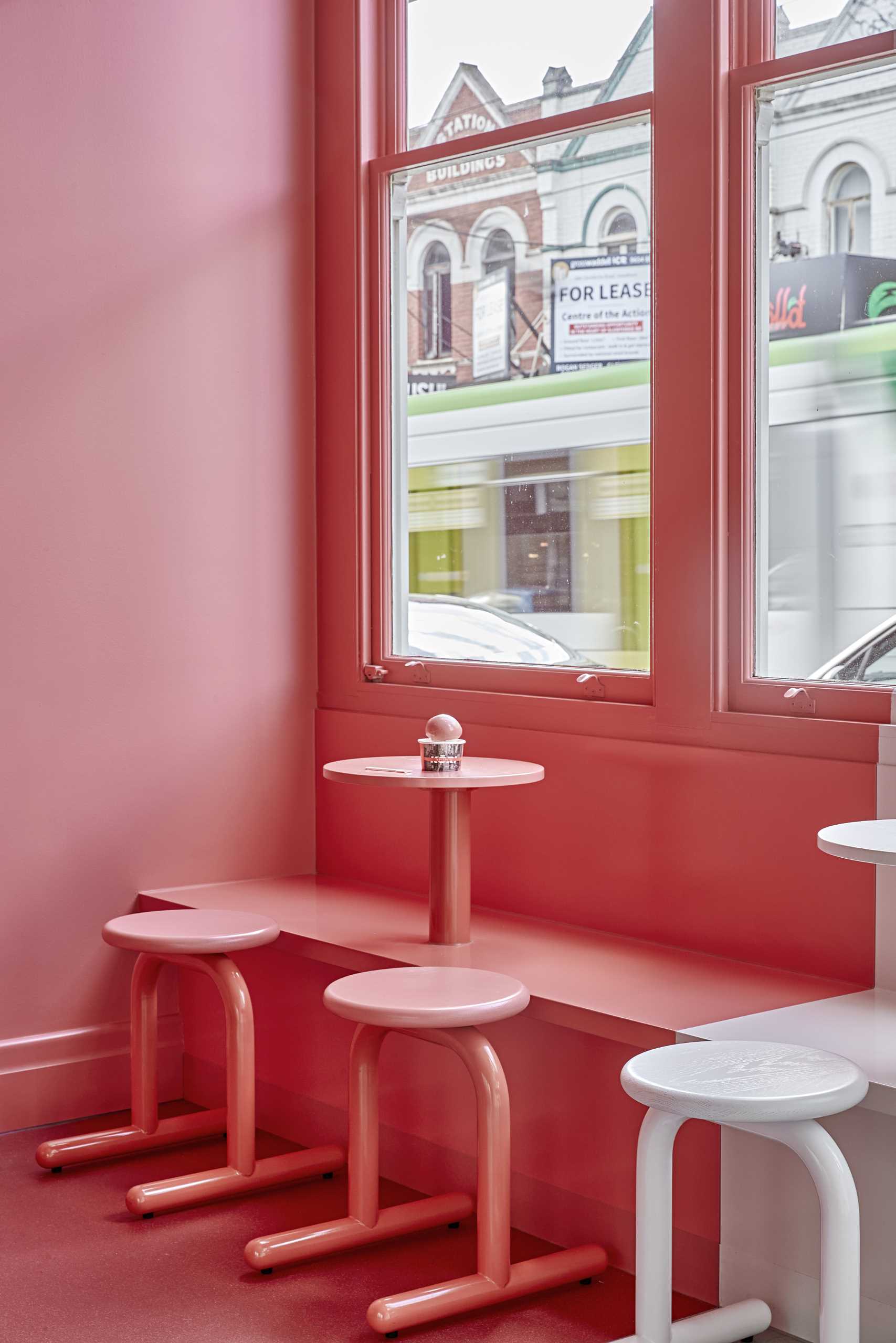 A modern ice cream shop with a matte pink and white interior, and seats by the window.