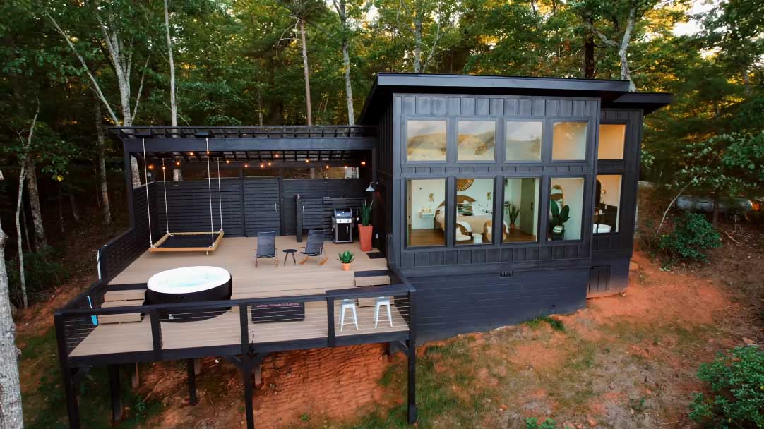 A modern cabin with black board and batten siding, and a large deck.