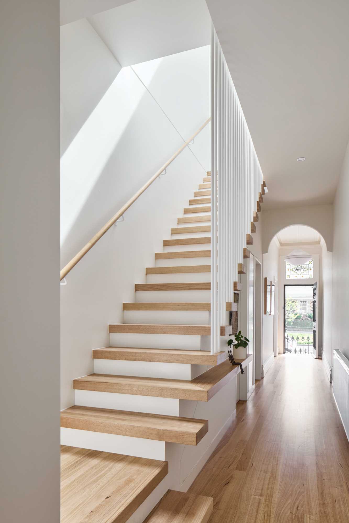 A modern white and wood staircase with a tread that turns into a shelf.