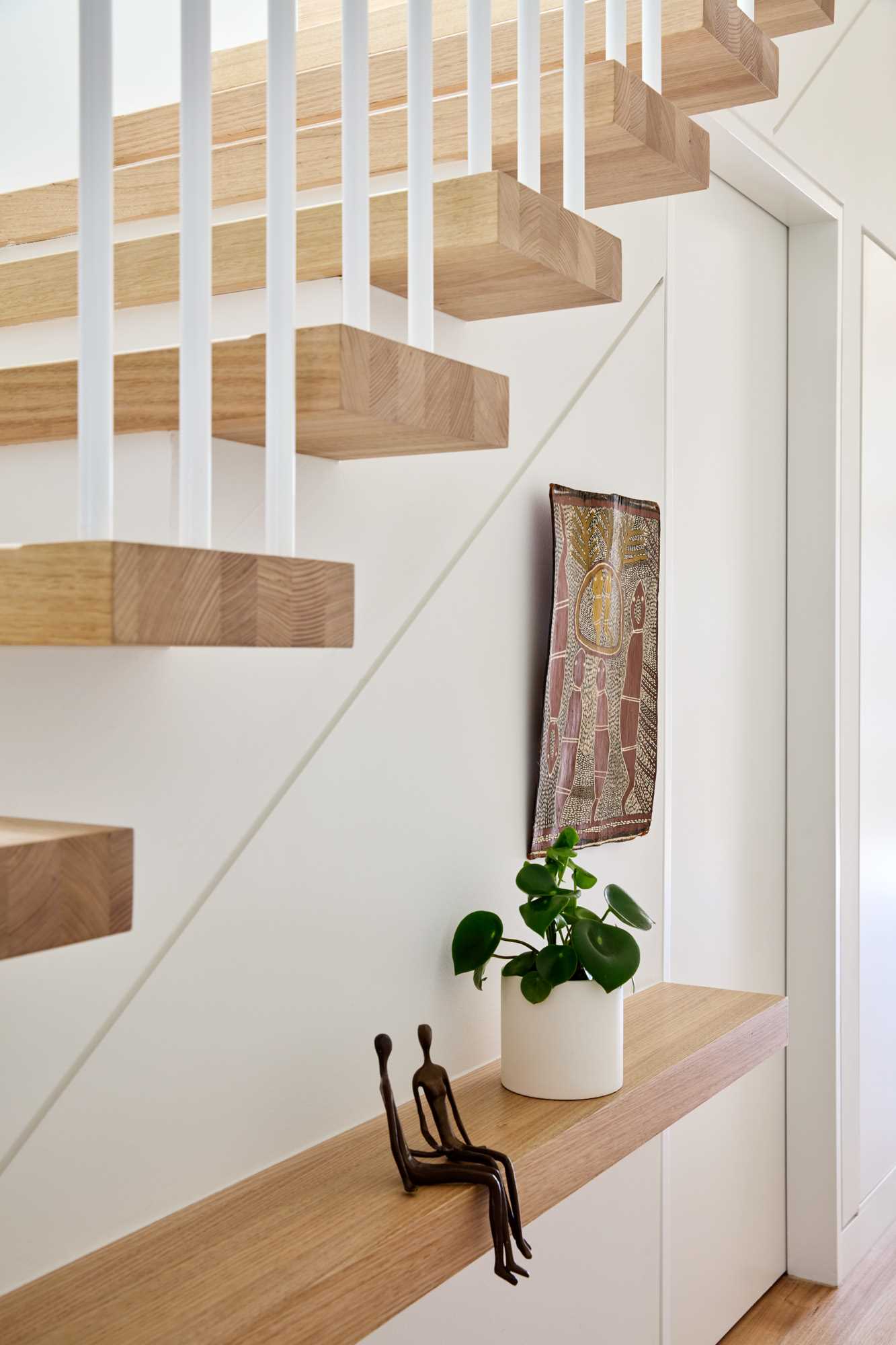 A modern white and wood staircase with a tread that turns into a shelf.