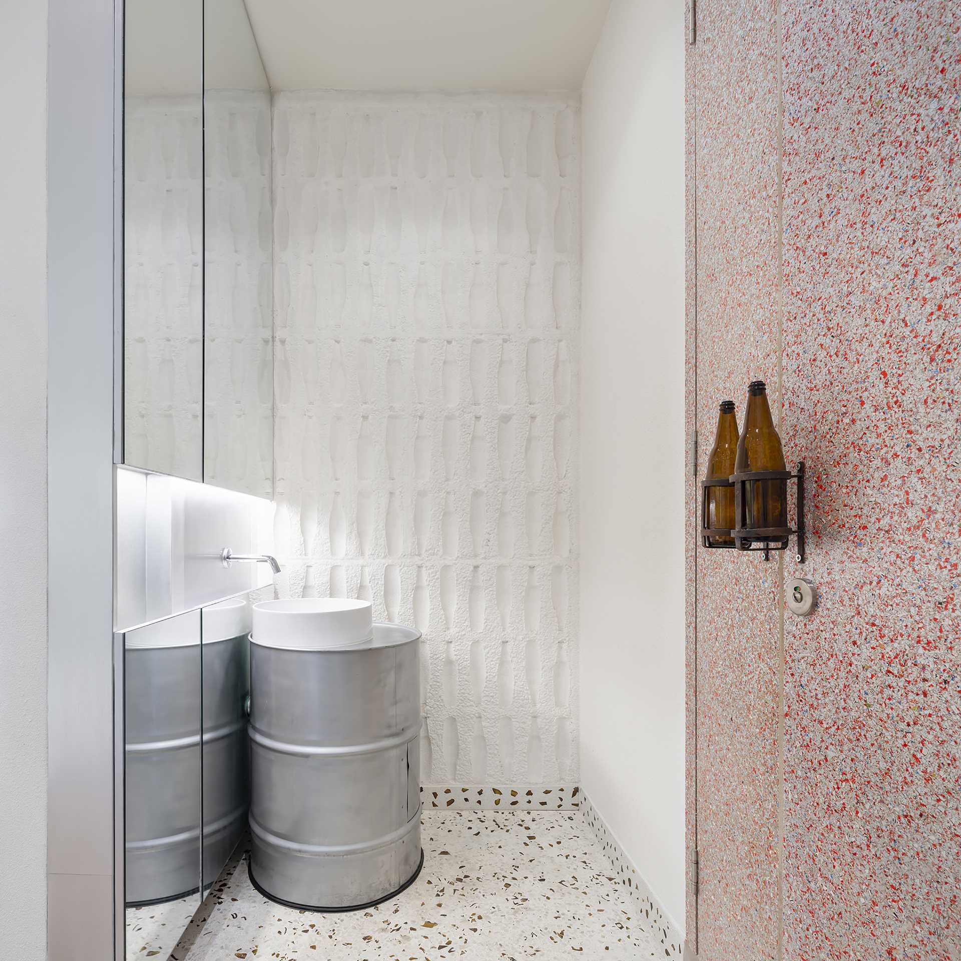 This cafe bathroom includes a used galvanized iron oil tank as a basin counter, and used glass bottles as a door knob.