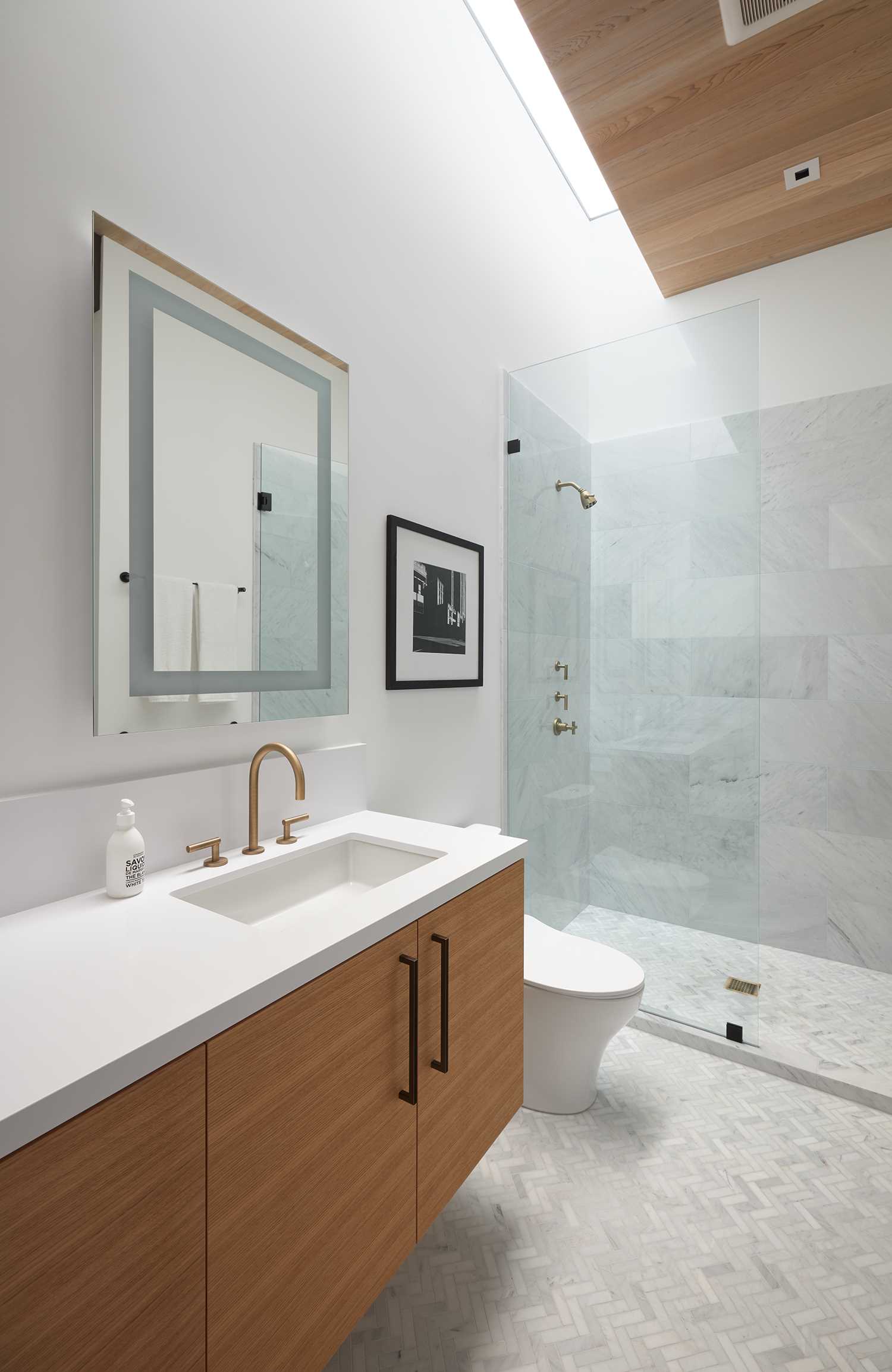 A modern bathroom with wood accents, light colored tiles, and a skylight.