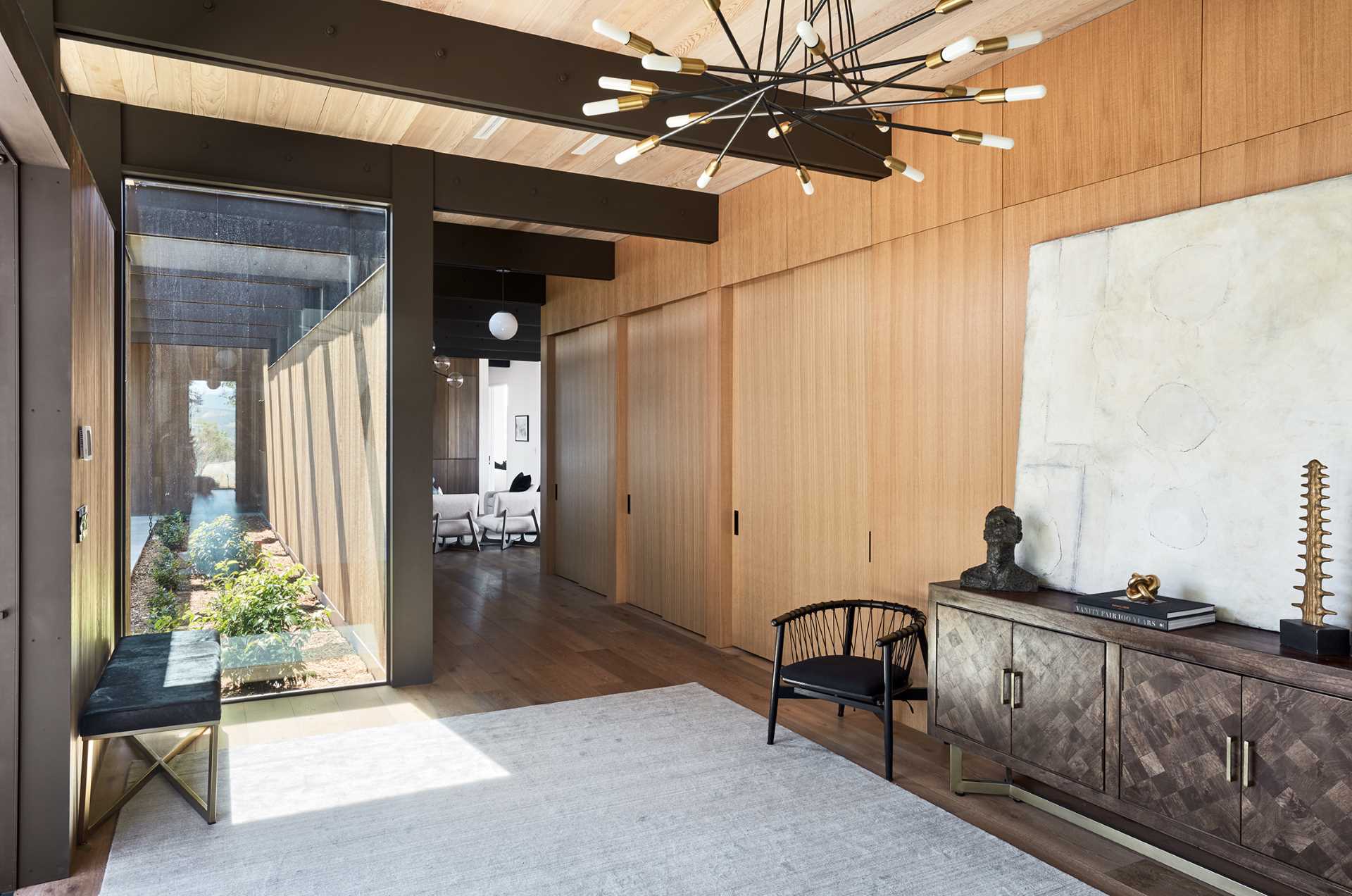 This modern entryway has a small bench area, as well as a sculptural chandelier and wood accent wall that allows collection of doors to blend in.