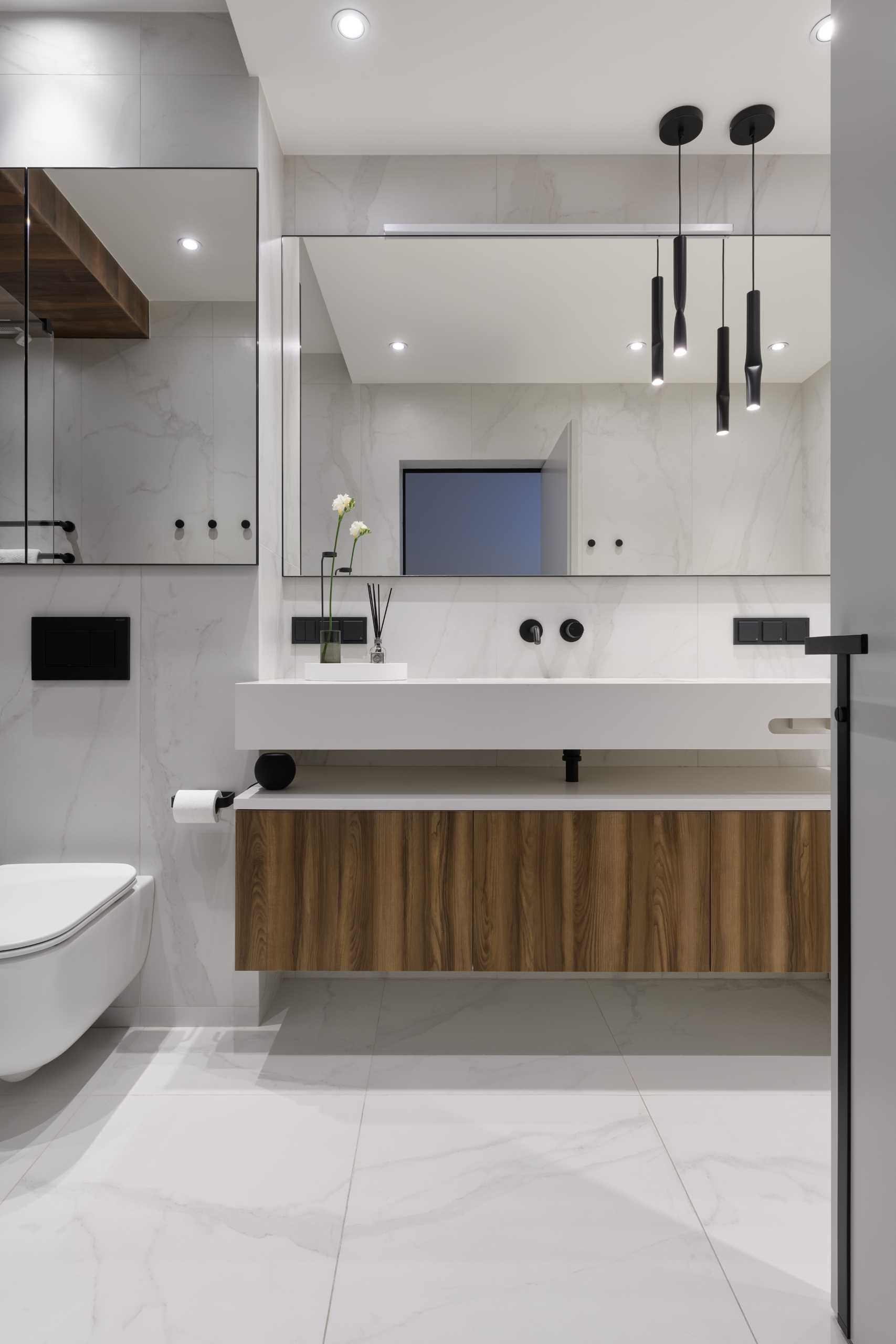 A modern bathroom includes a floating wood and white vanity, a bathtub that perfectly fits between the walls, and a walk-in shower.