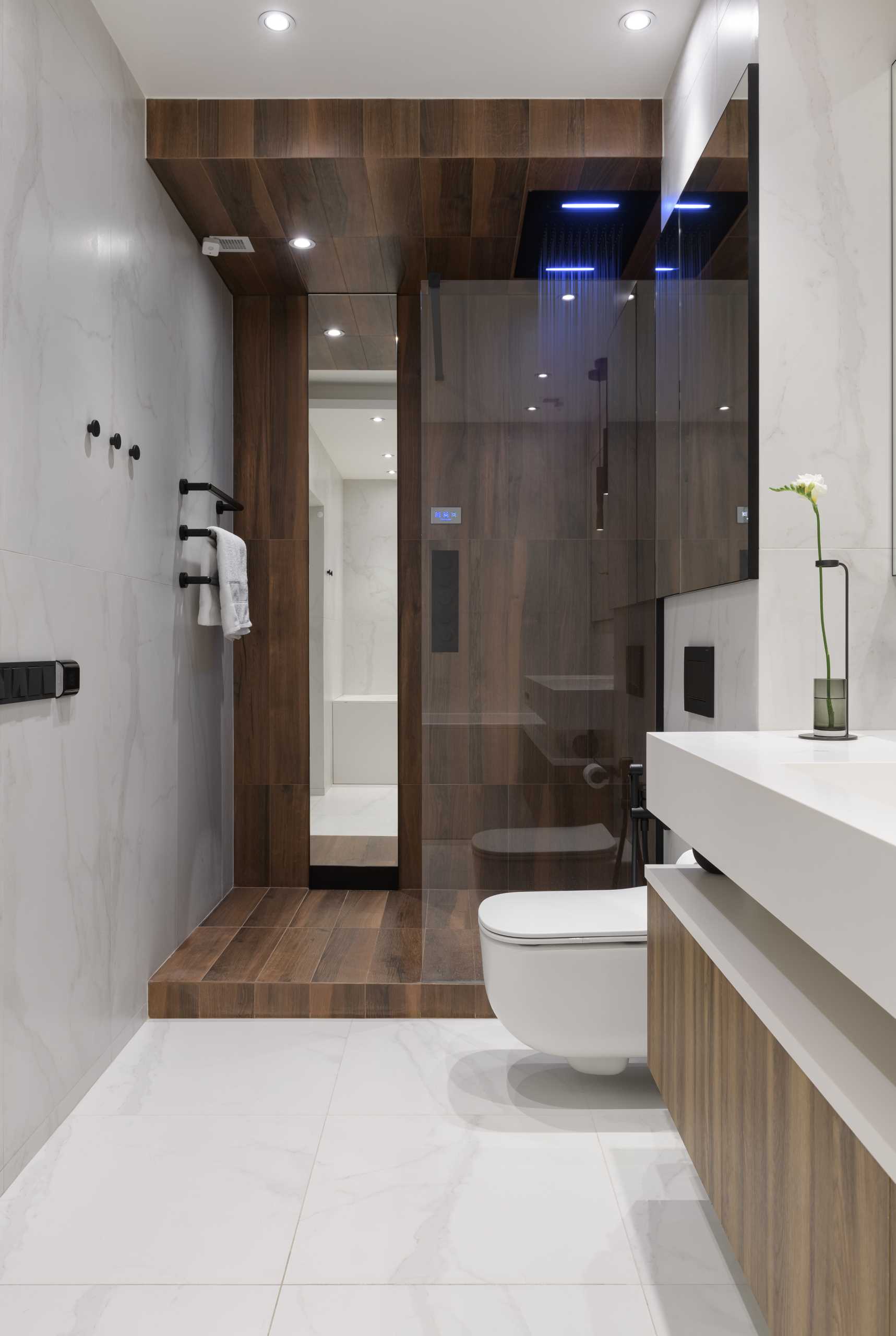 A modern bathroom includes a floating wood and white vanity, a bathtub that perfectly fits between the walls, and a walk-in shower.