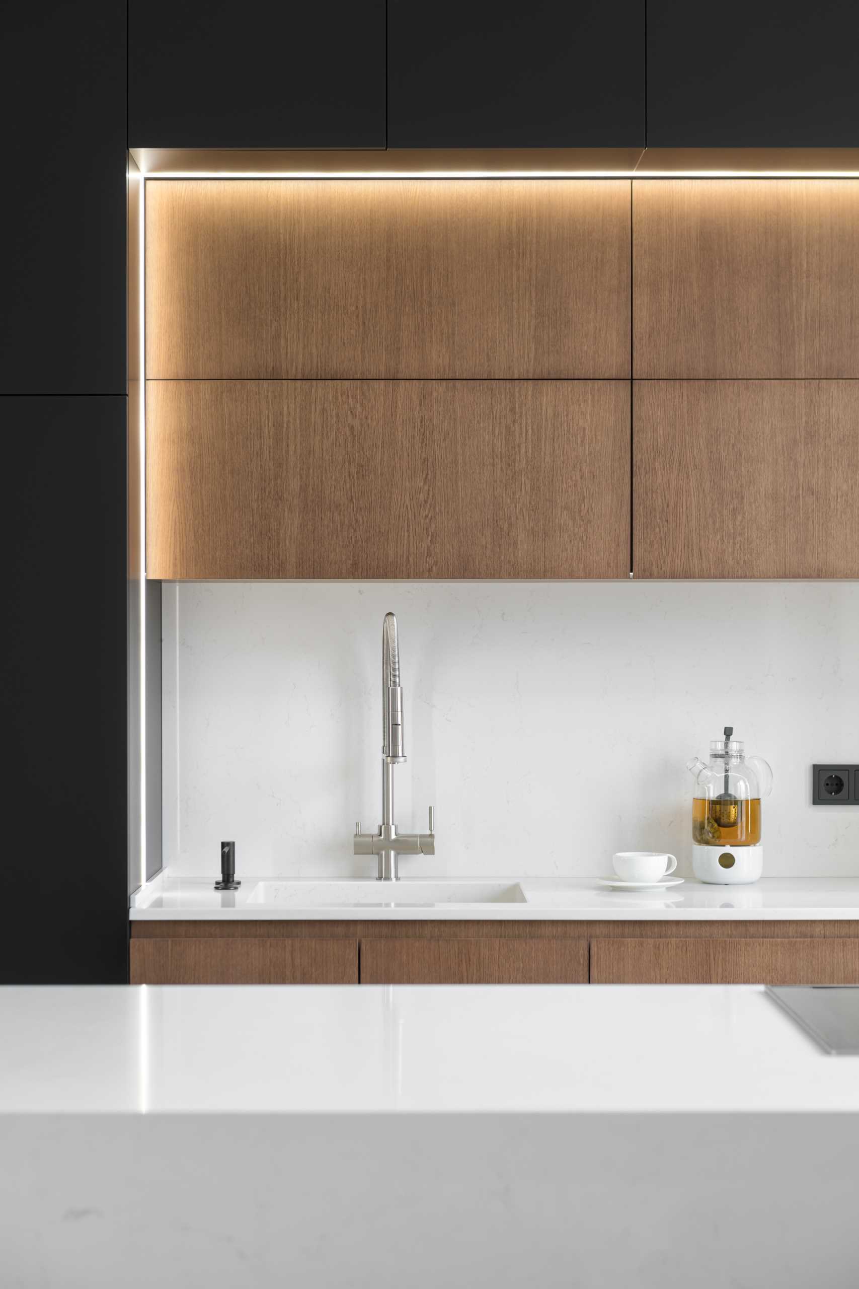 A modern kitchen with black, wood, and white cabinets, and hidden lighting.