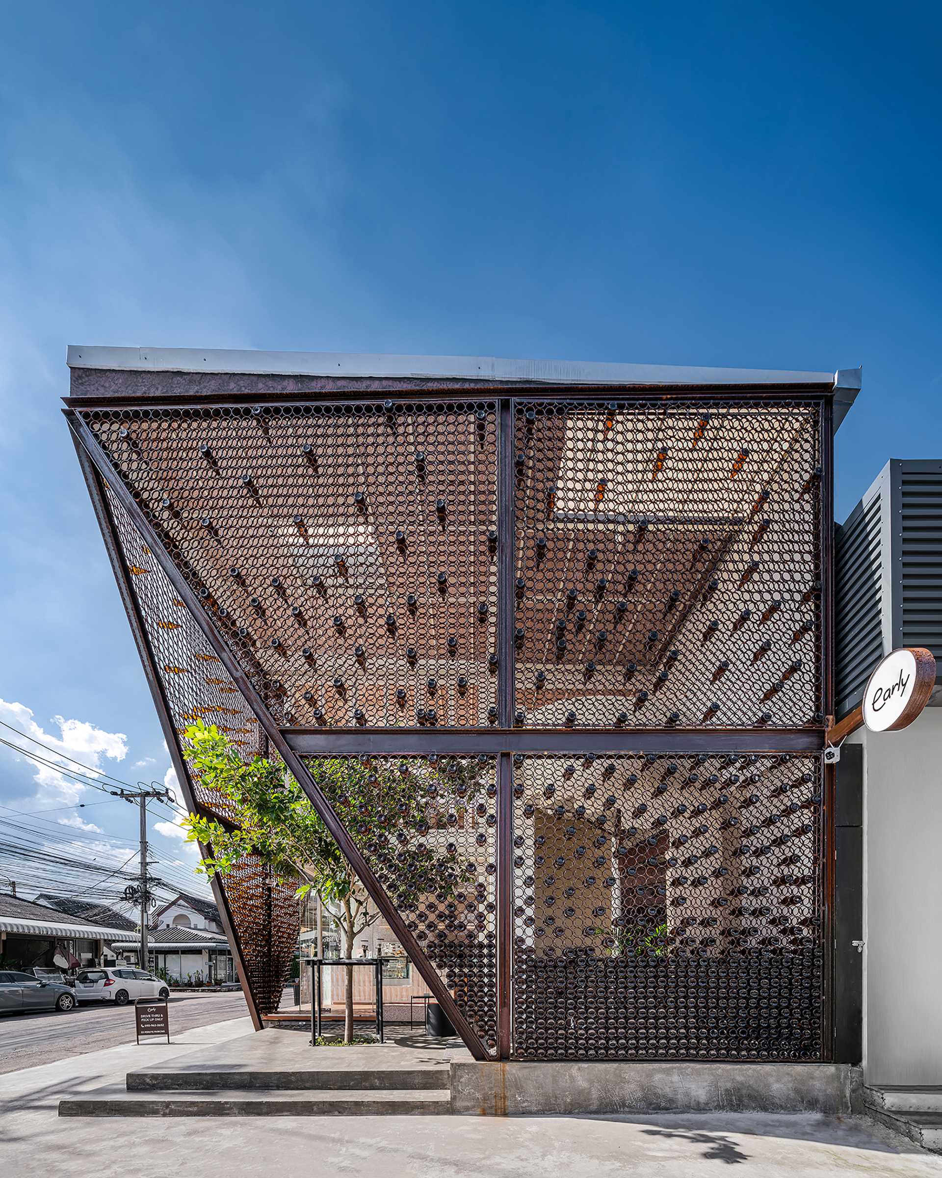 A modern cafe with a facade that features metal rings that hold recycled beer bottles.