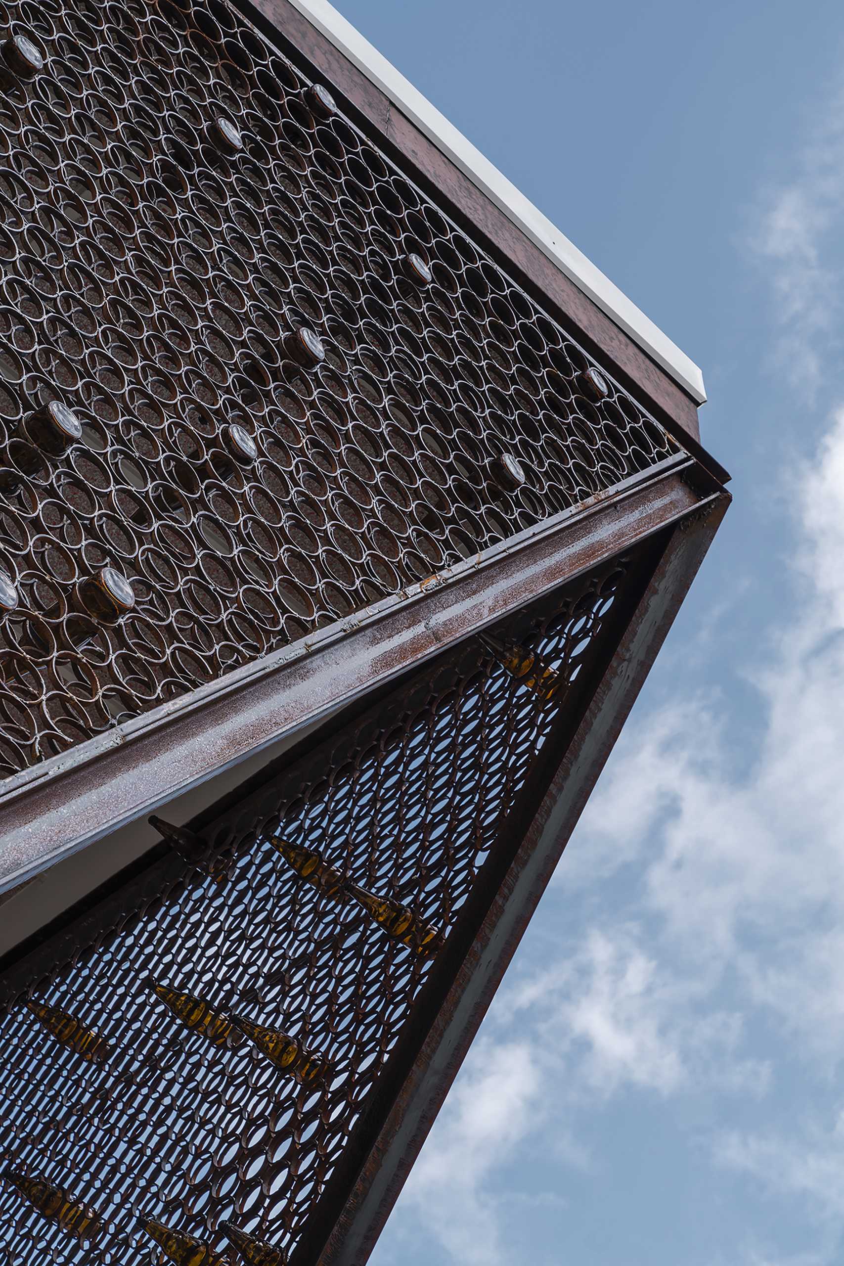 A modern cafe with a facade that features metal rings that hold recycled beer bottles.