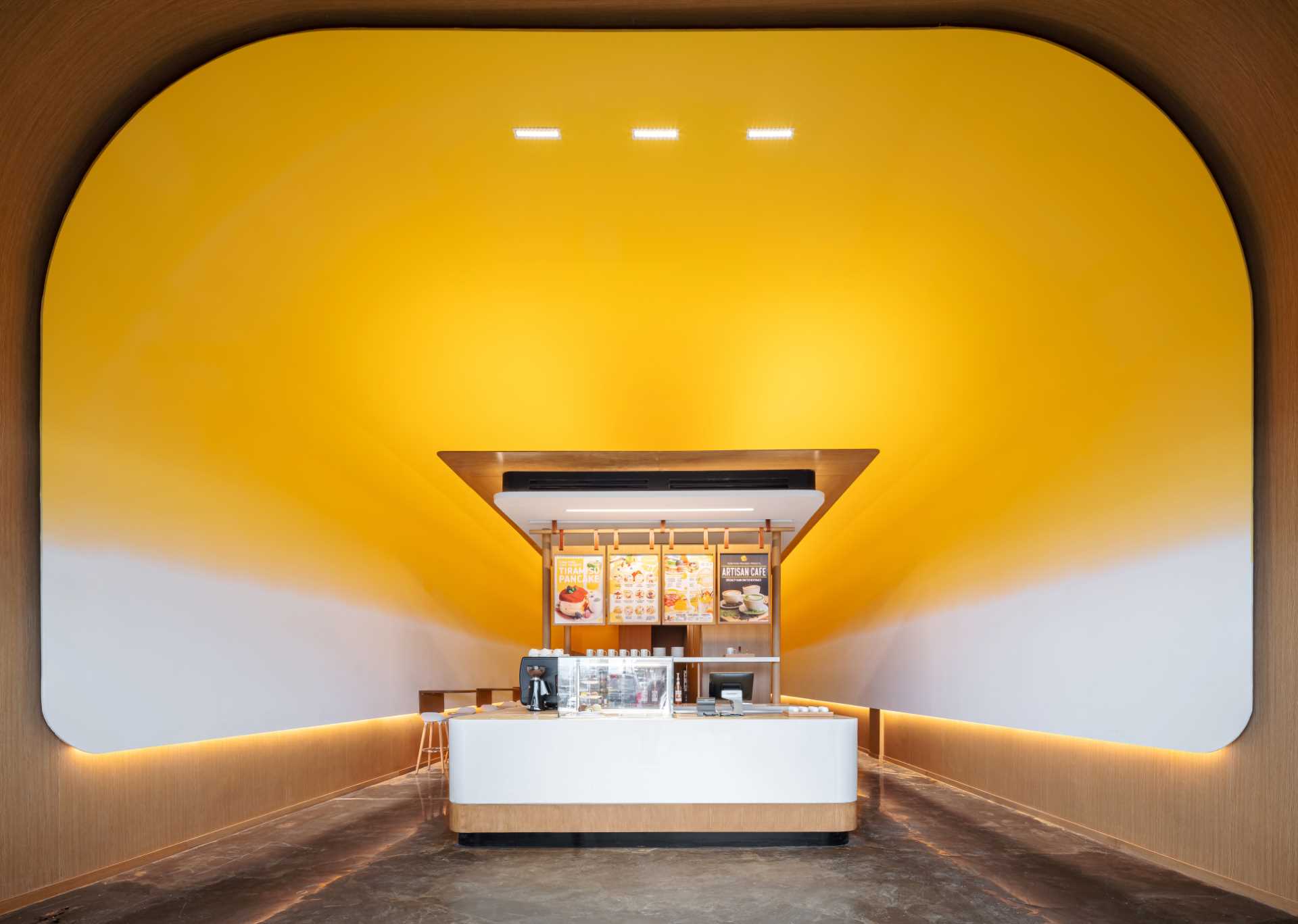 Visitors to this modern cafe are greeted by the soft curve and bright yellow of the high ceiling as it frames a modern temple-like structure.