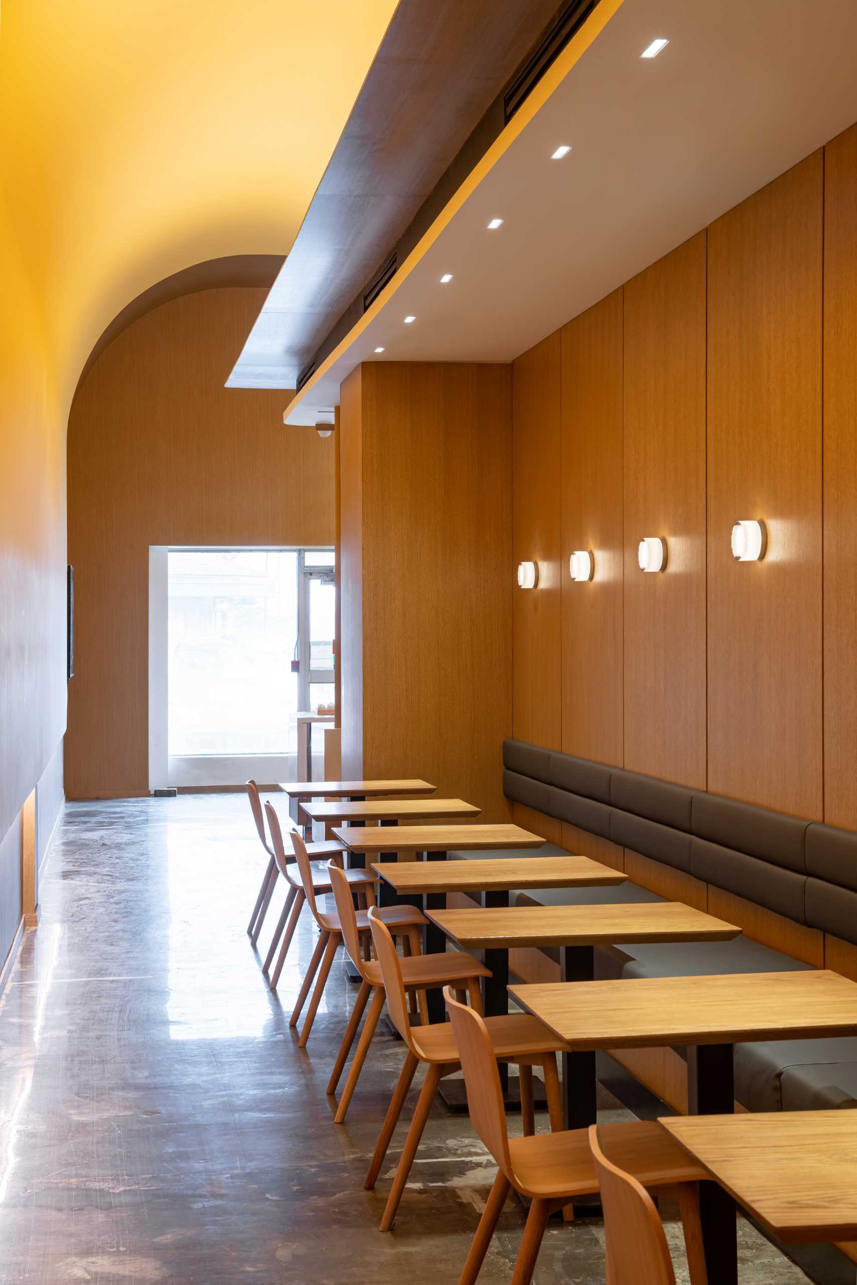 A modern cafe with upholstered banquette seating, wood tables and chairs, and banquette seating.