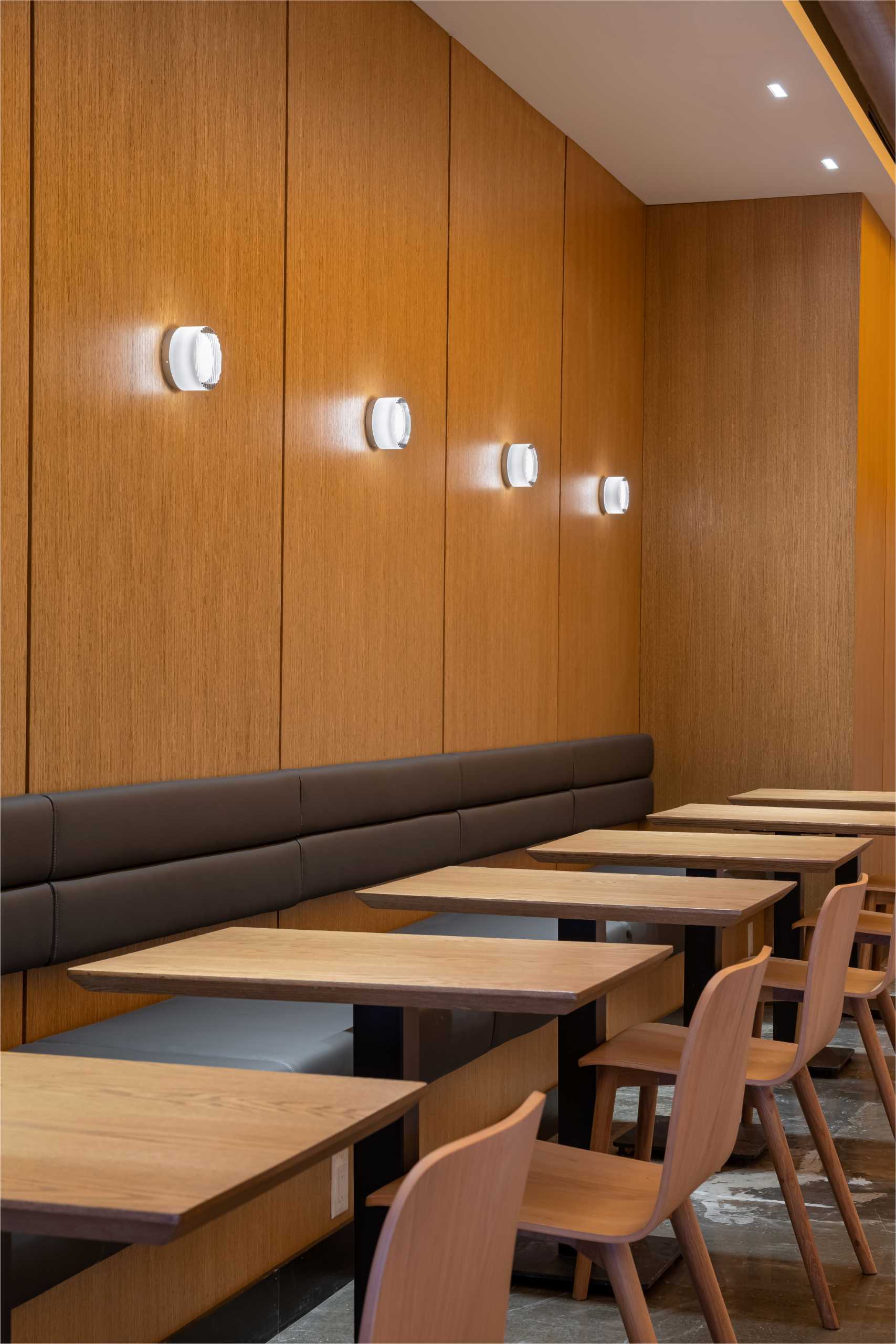 A modern cafe with upholstered banquette seating and wall sconces.