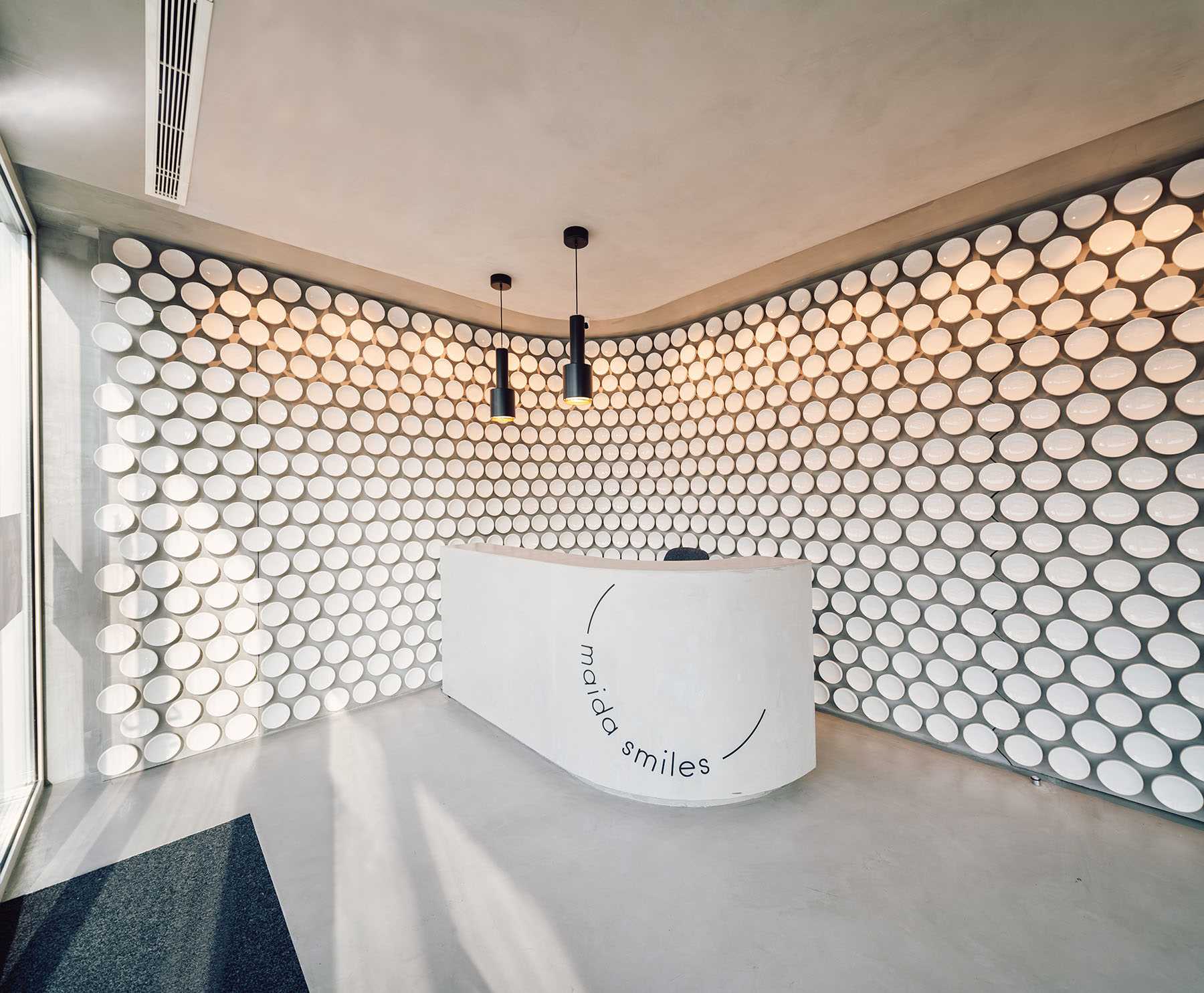 Mais de 500 discos de cerâmica feitos à mão revestem a parede desta moderna clínica odontológica, enquanto o microcimento cobre o chão.