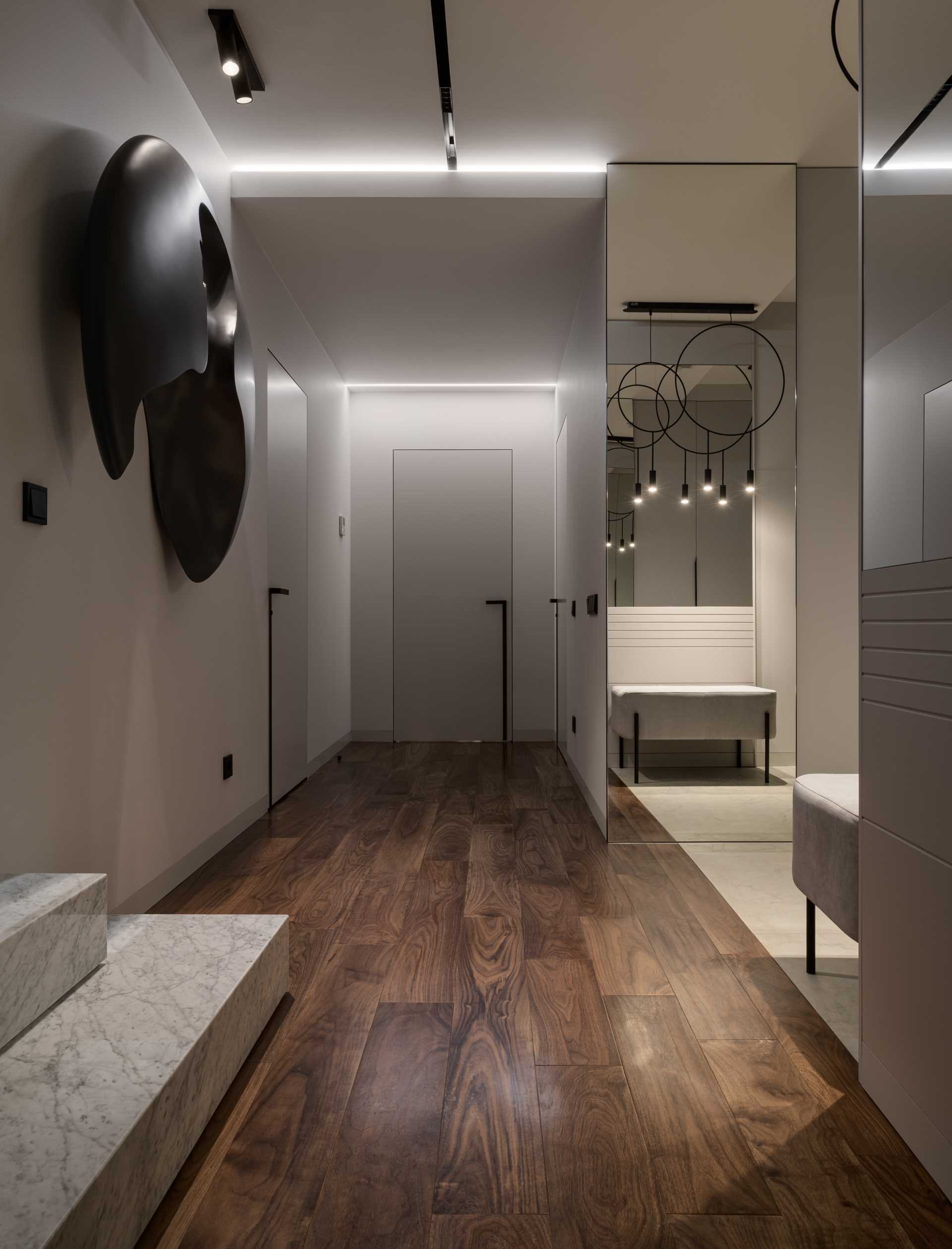 A modern entryway with a full-length mirror, wood flooring, a bench, and a wall sculpture.