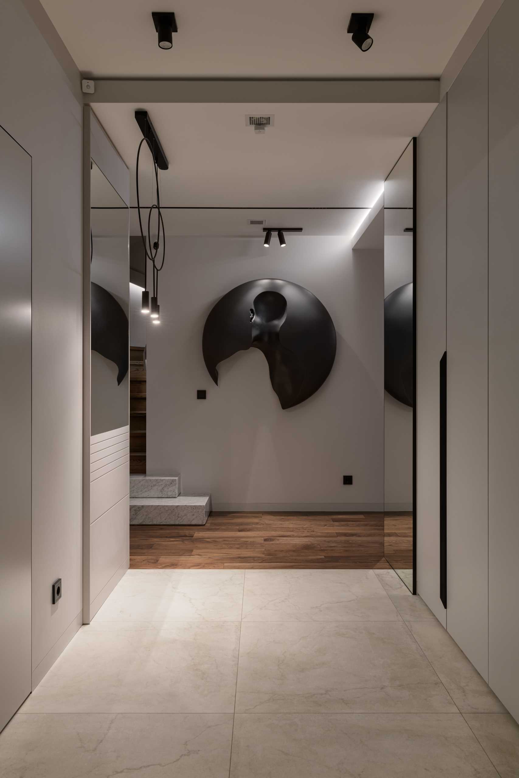 A modern entryway with a full-length mirror, wood flooring, a bench, and a wall sculpture.