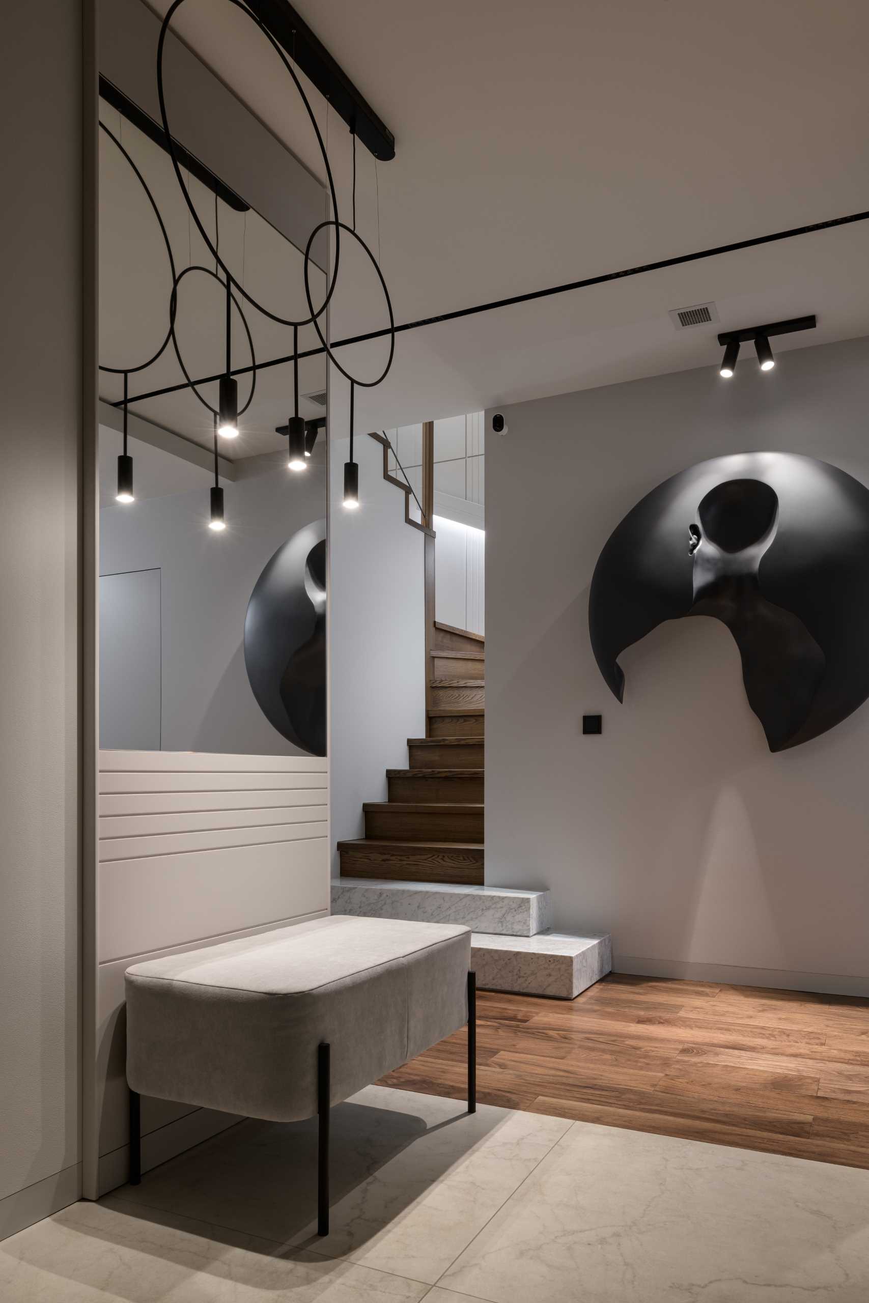 A modern entryway with wood flooring, a bench, and a wall sculpture.