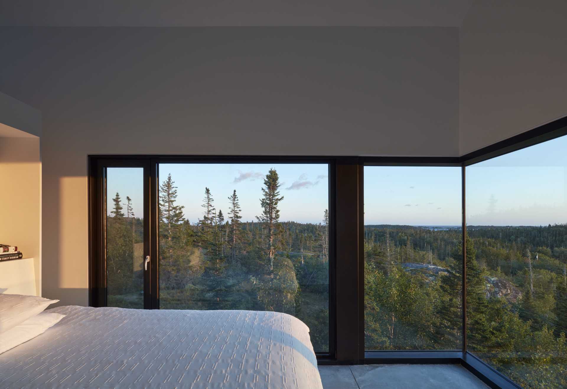 In this modern bedroom, the wrap-around black-framed windows showcase the uninterrupted view of the trees.