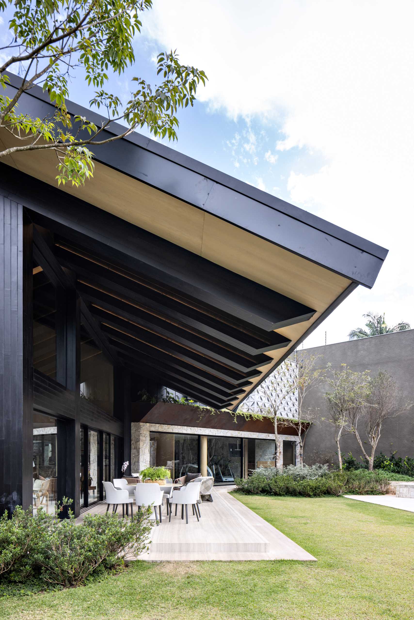 A remodeled home includes a large roof that overhangs a patio, and showcases the structure of the house.