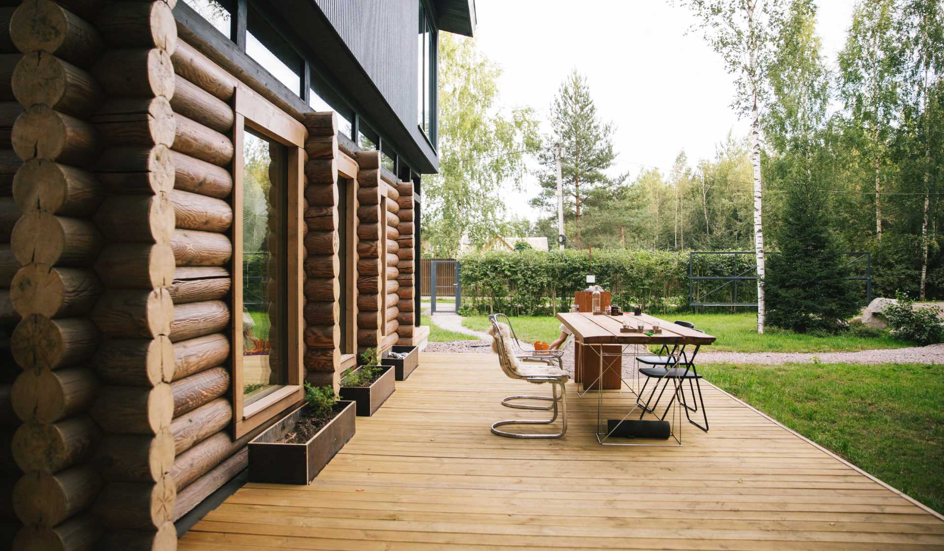 A log home topped with a modern black upper floor, and also includes a deck for outdoor dining.