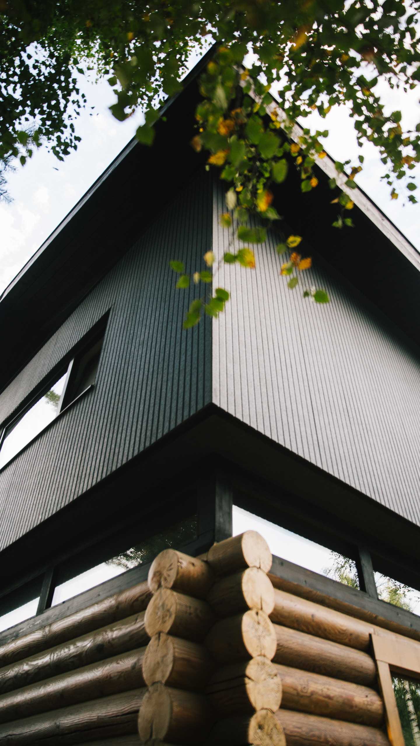 A modern log home with a modern black second floor and roof, and a band of windows.