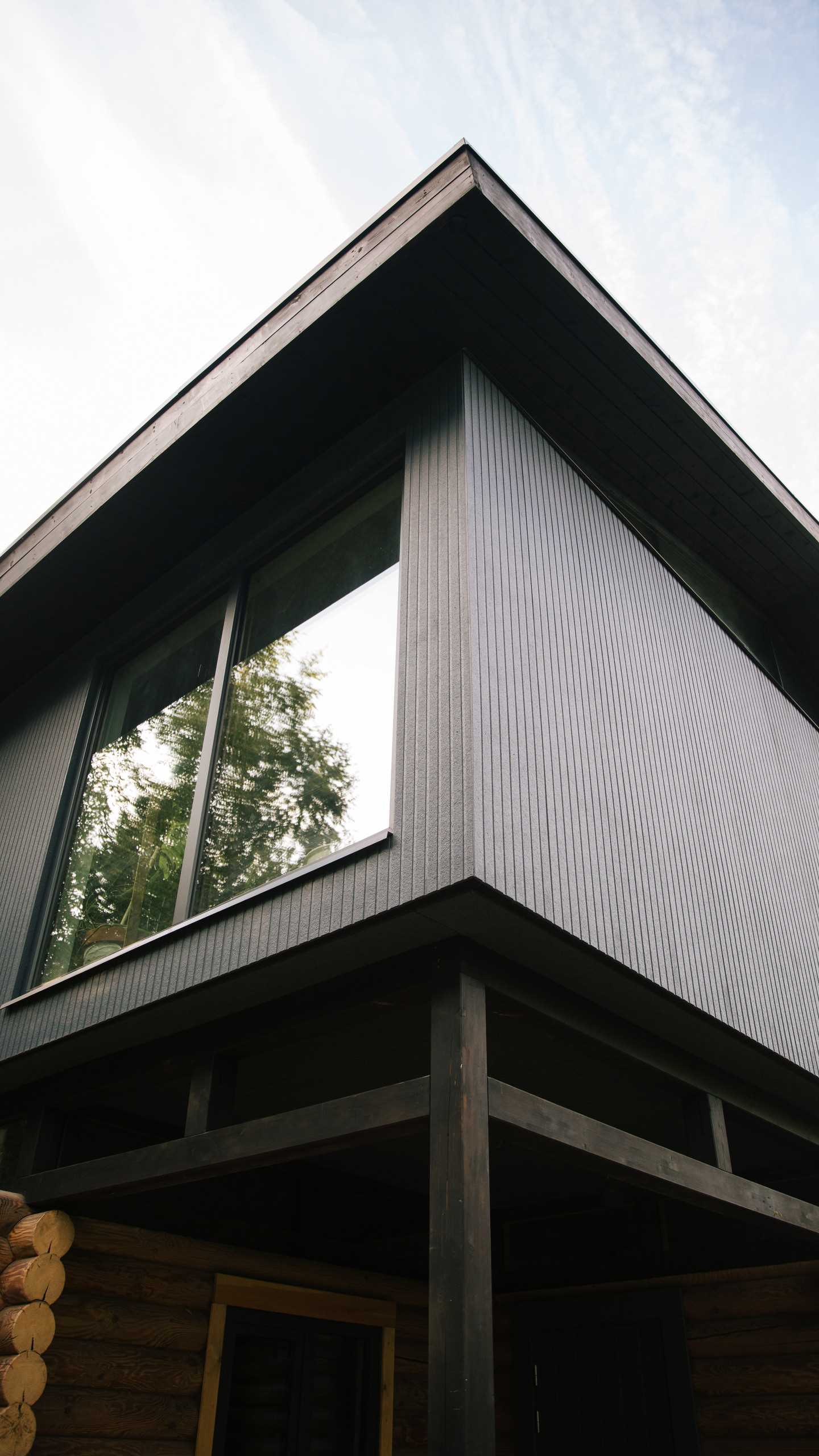 A modern log home with a modern black second floor and roof, and a band of windows.