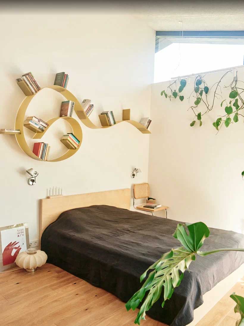 Một phòng ngủ hiện đại với đồ nội thất tối thiểu và giá sách cong treo tường.