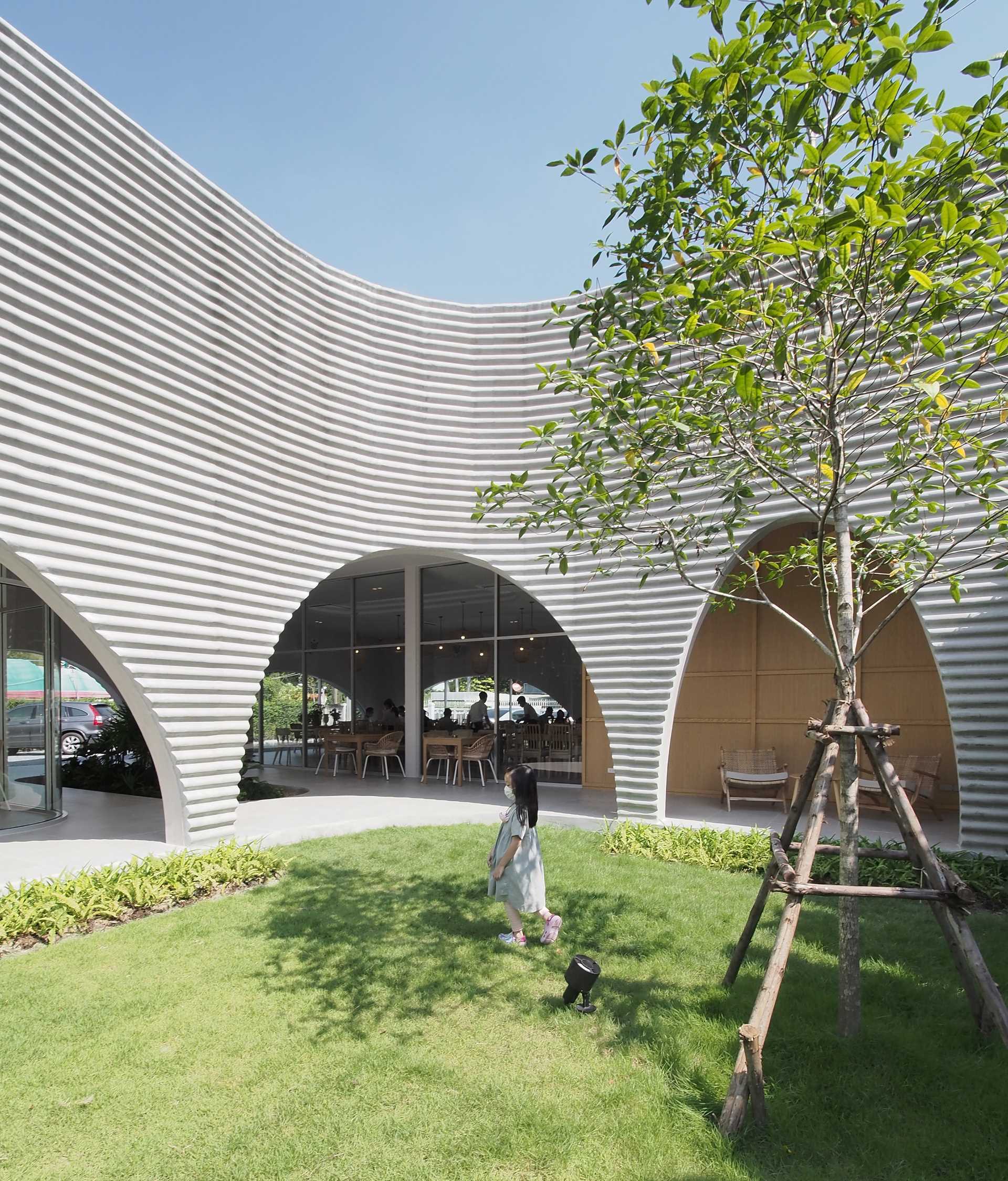 A modern restaurant and cafe with a wavy pre-case concrete facade and arched openings.