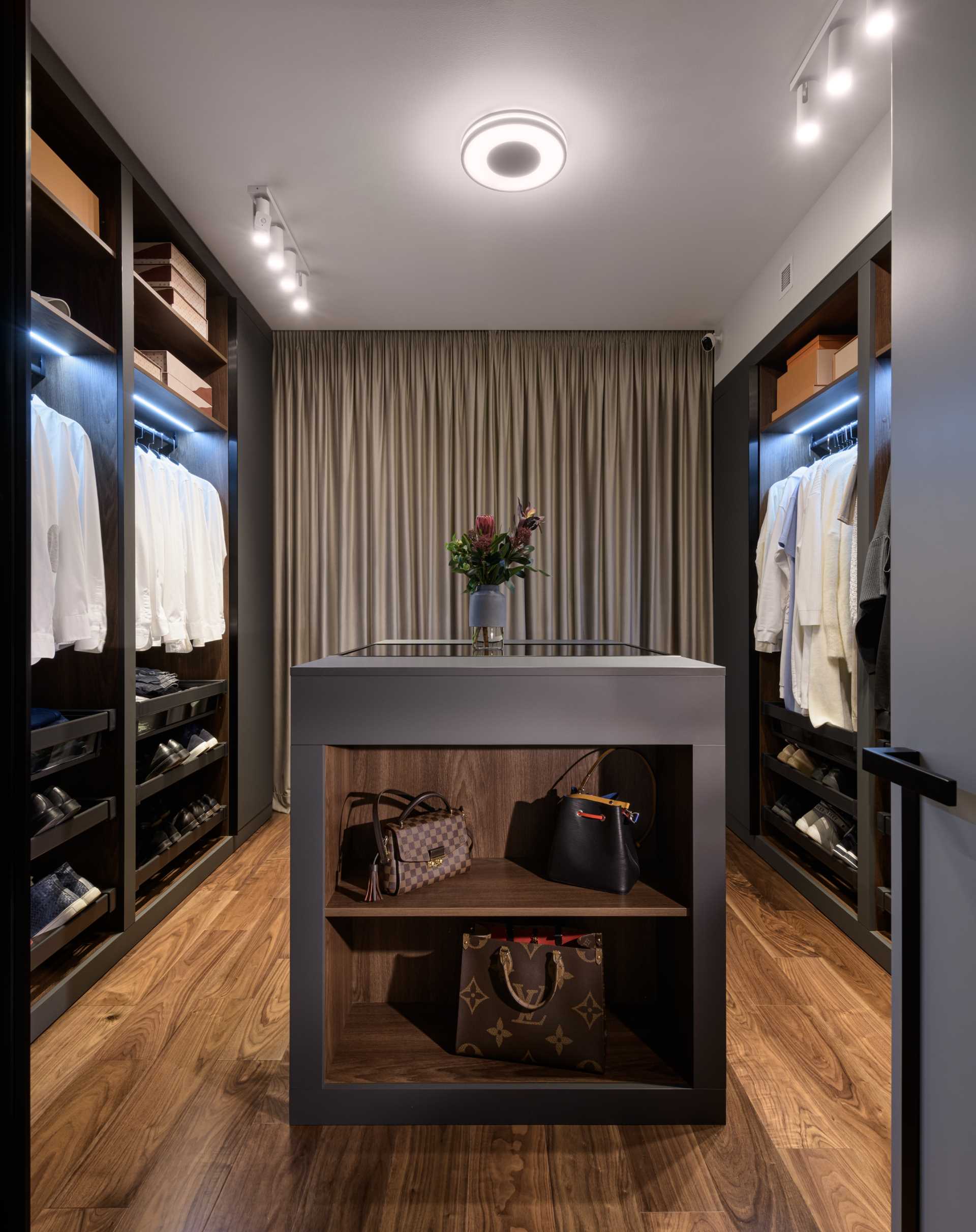 A walk-in closet has a central island filled with storage for accessories, while the walls are dedicated to clothing and shoe storage.
