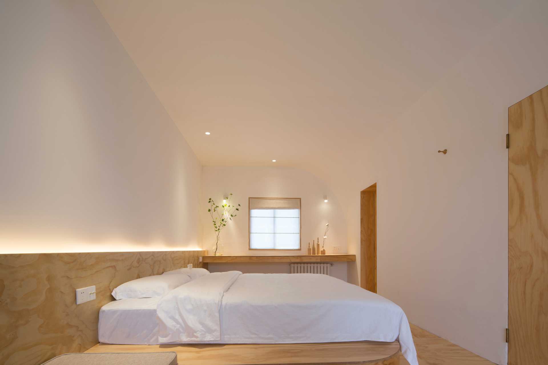 A modern bedroom with a full-width headboard, LED lighting, and a curved ceiling.