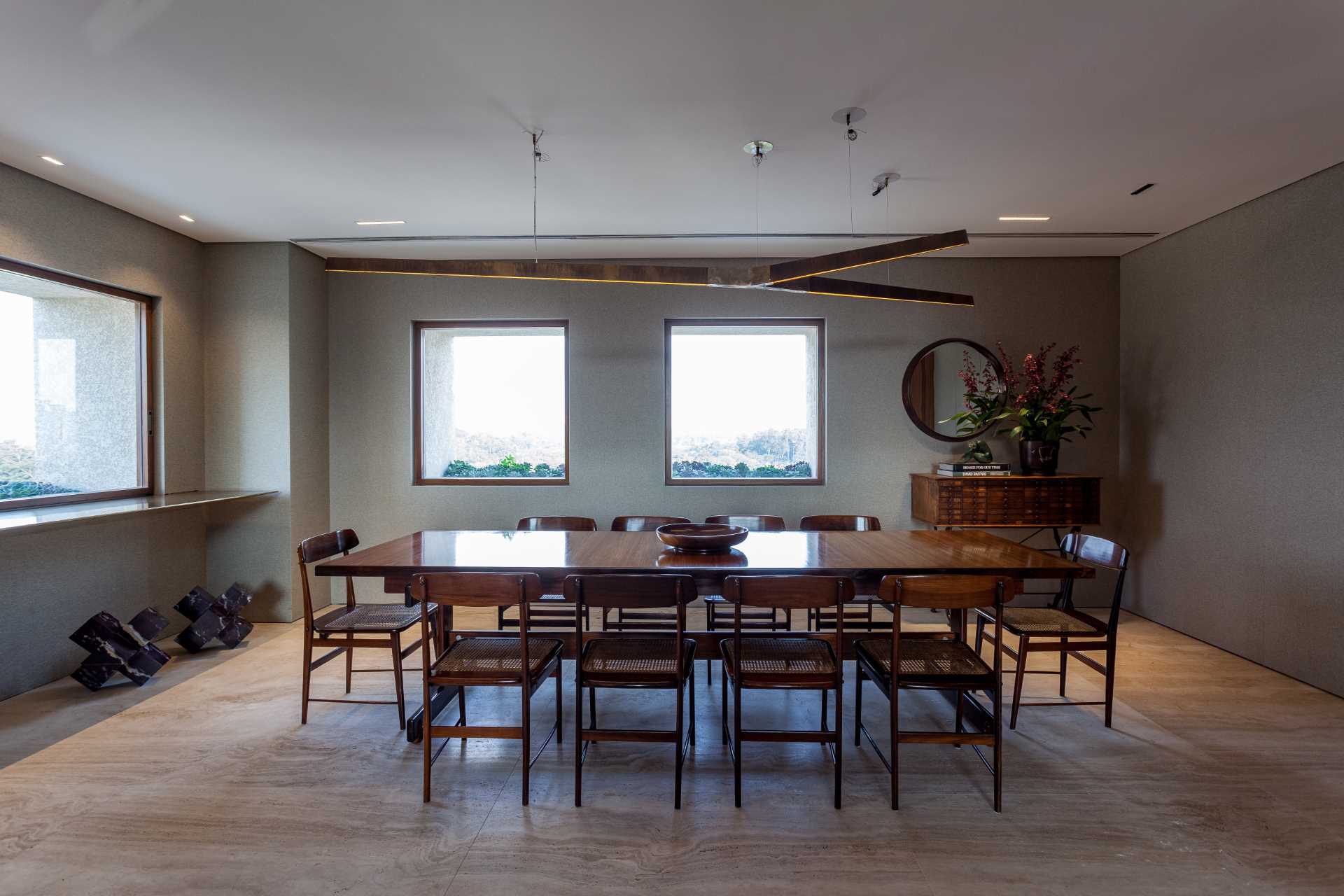 The dining room includes a large wood table and surrounding chairs designed by Sergio Rodrigues, while the floor is Roman Travertine Marble.