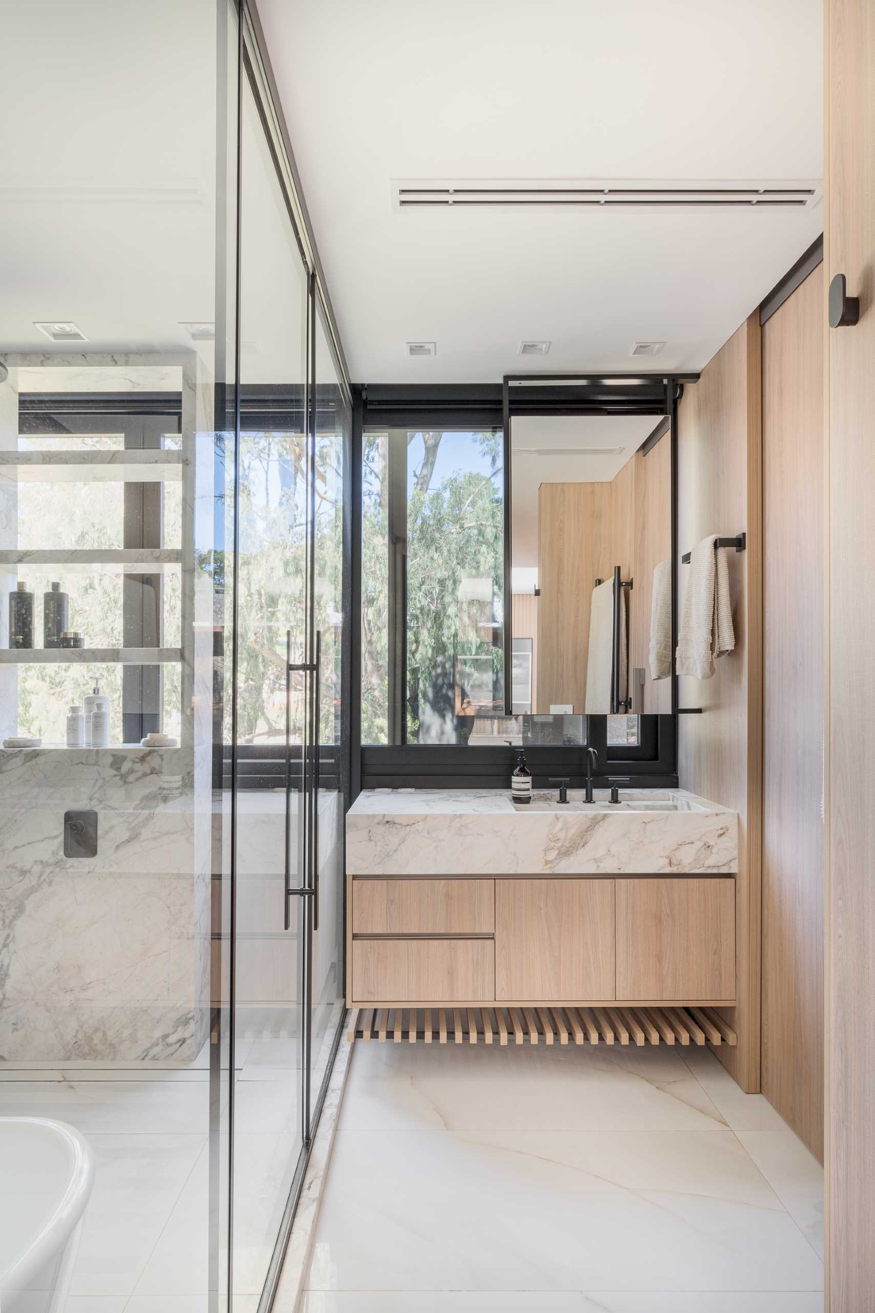 In this modern bathroom, there's a glass-enclosed wet room with a shower and freestanding bathroom, while the vanity area looks out to the treetops.