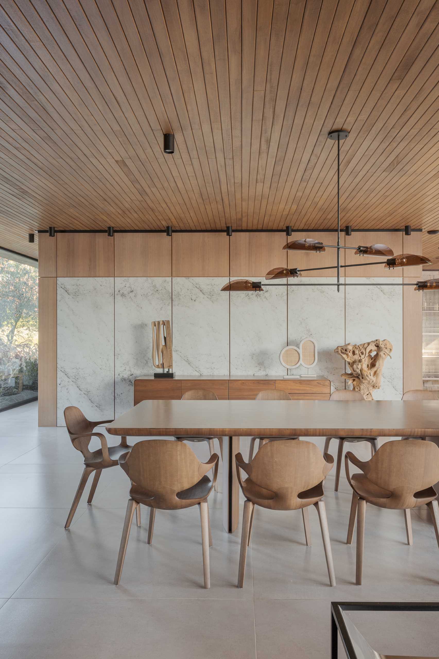 A built-in cabinet with glass doors stores complements this modern dining area, while the wall features stone panels and a wood sideboard.