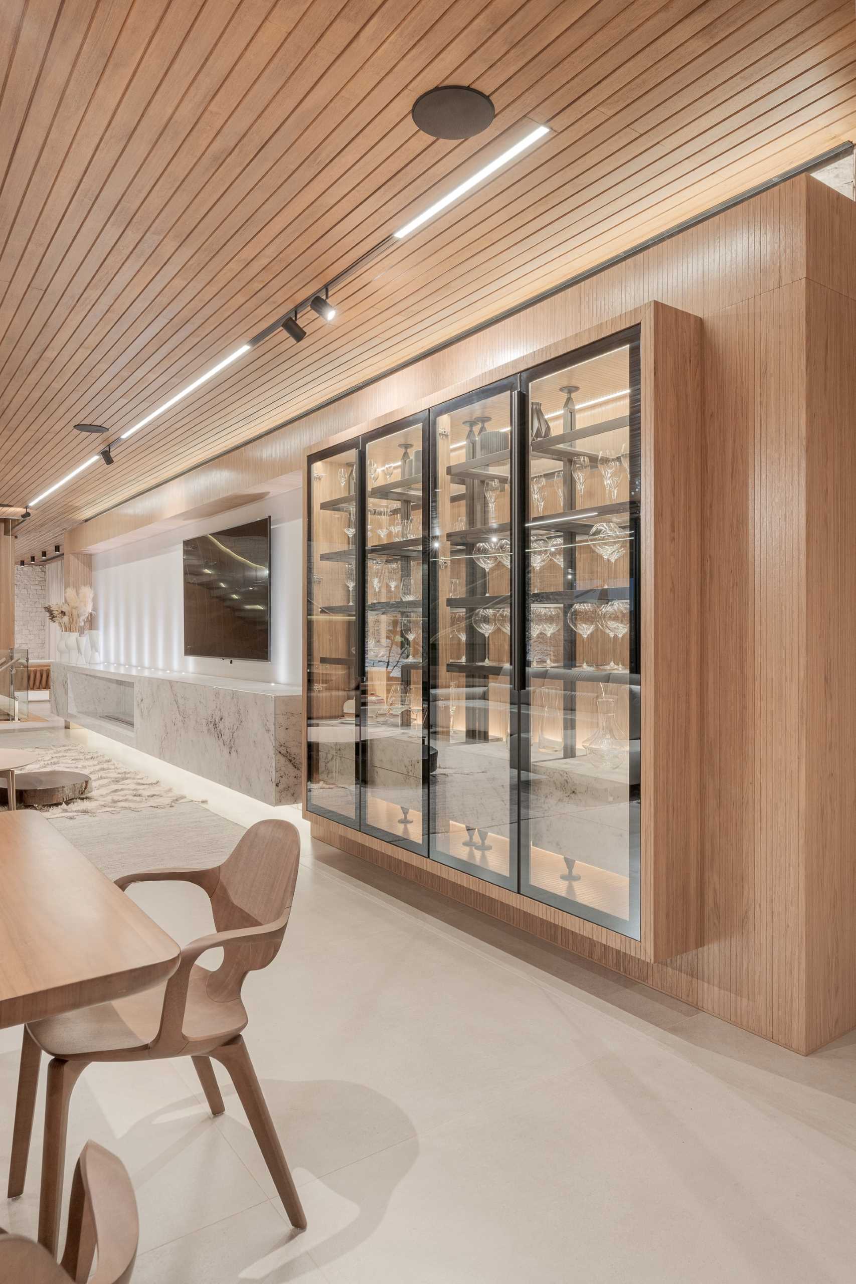 A built-in cabinet with glass doors stores complements this modern dining area, while the wall features stone panels and a wood sideboard.