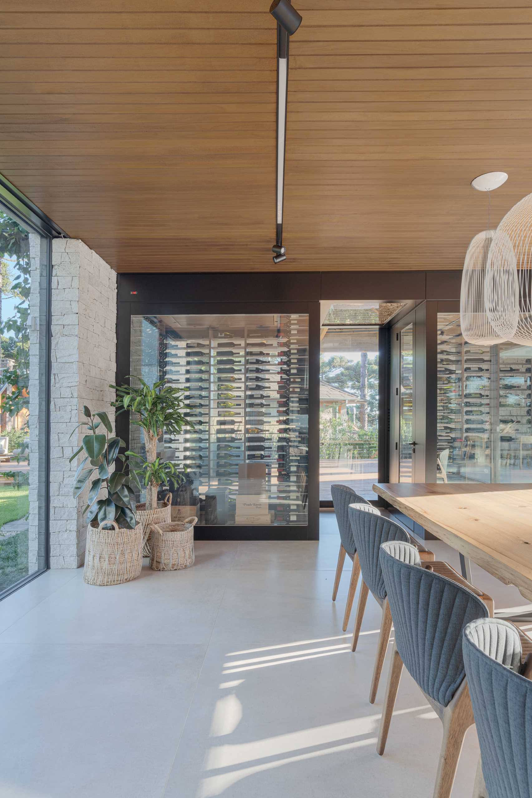 A modern dining area with a long wood table connected to the kitchen island. Dark grey chairs provide a contrasting element, while the wall at the end of the table is dedicated to a pair of glass enclosed wine cellars.