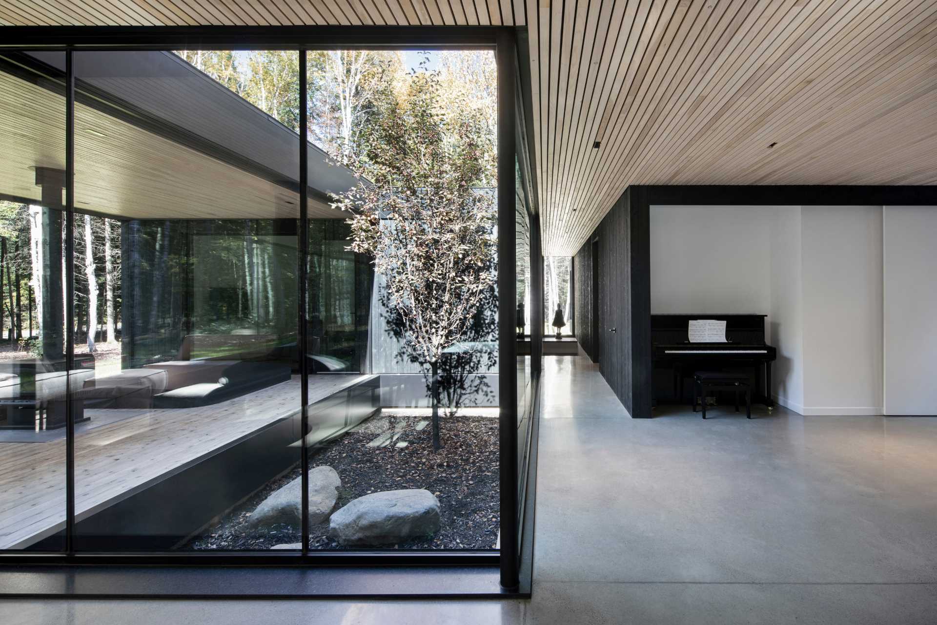 A modern hallway with black details, floor-to-ceiling windows, concrete floors, and wood ceiling.
