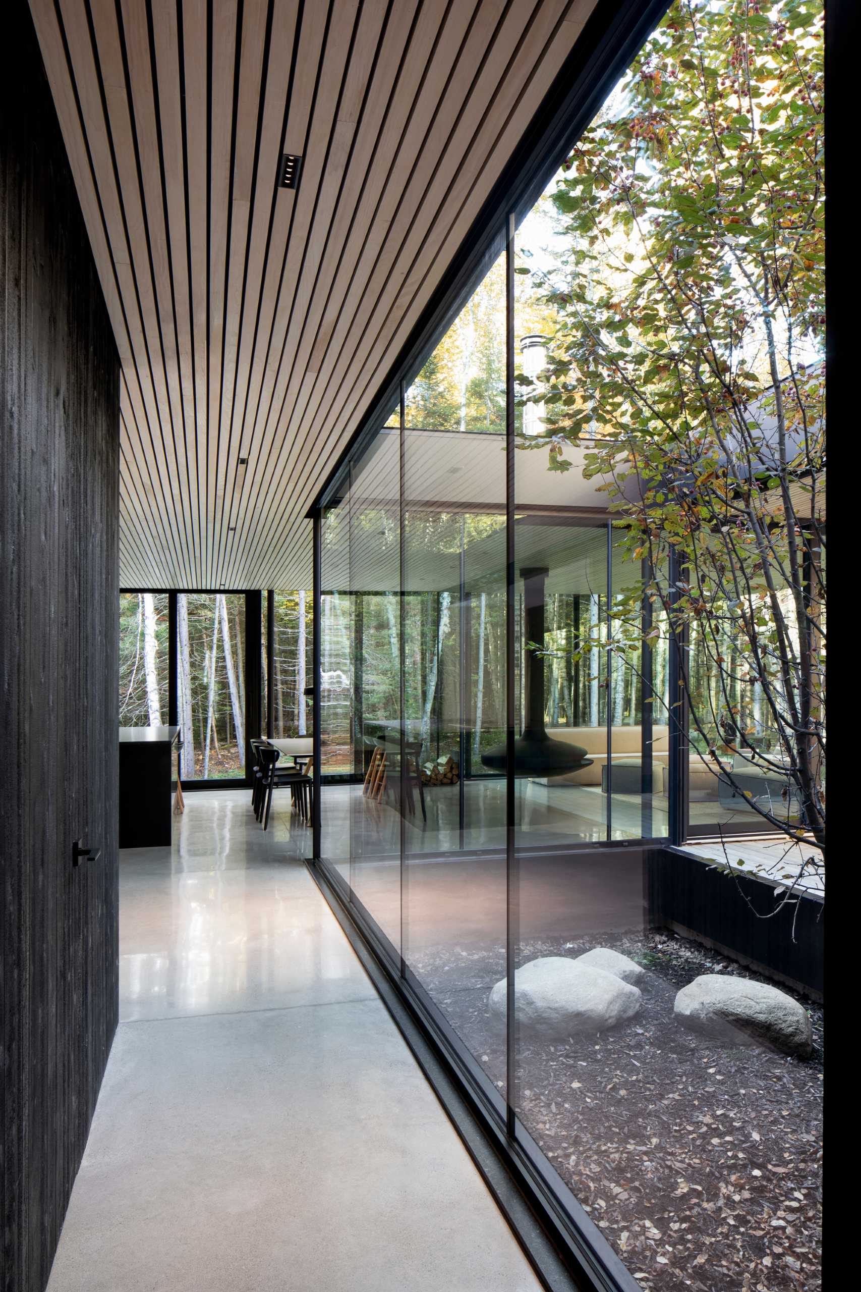 A modern hallway with black details, floor-to-ceiling windows, concrete floors, and wood ceiling.